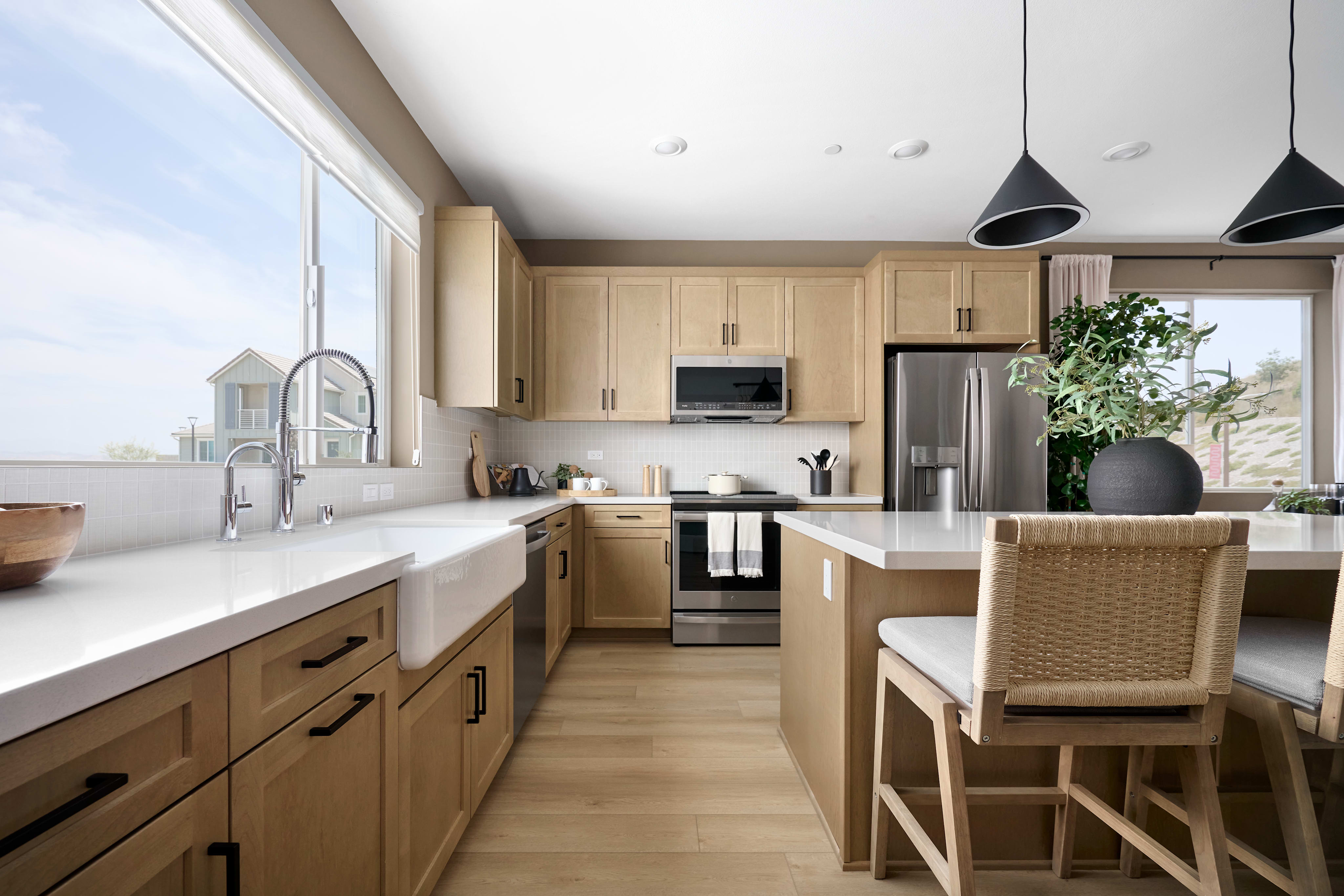A modern kitchen with a large sink and island in the foreground, and light wood cabinets and stainless steel appliances in the background.