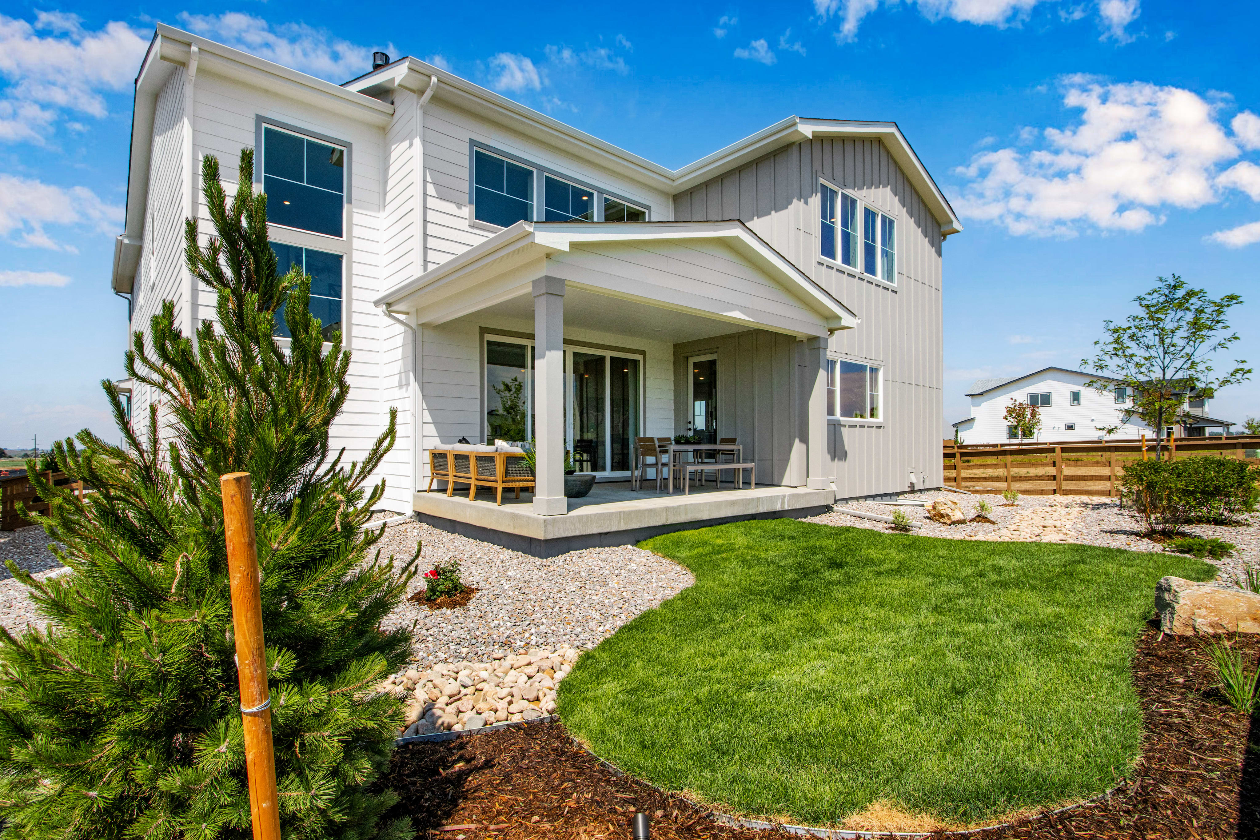 A modern house with a covered patio and green lawn is set against a bright blue sky with scattered clouds.