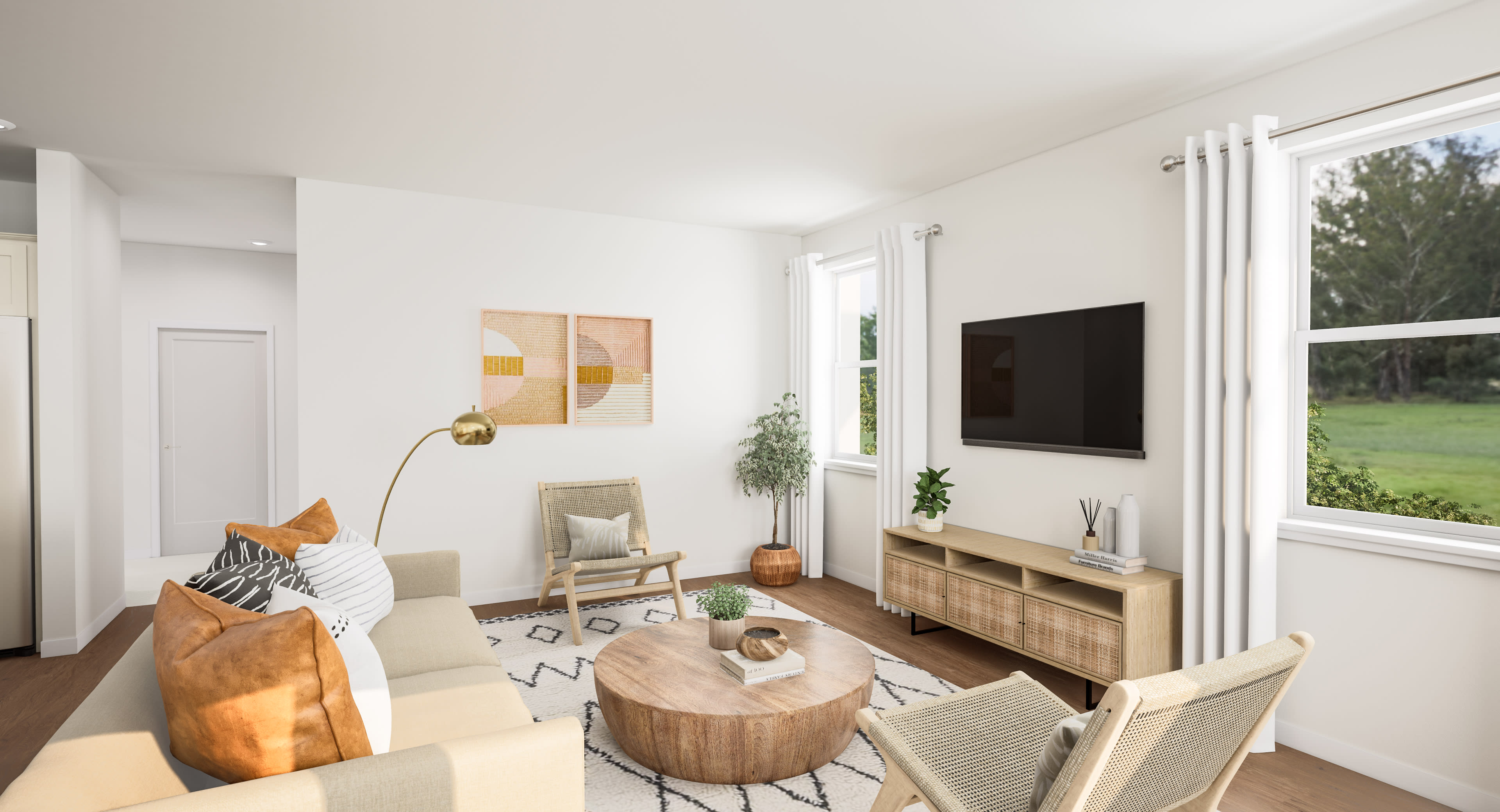 A modern living room with a beige sofa and a round wooden coffee table in the foreground, and a television and windows overlooking a green landscape in the background.