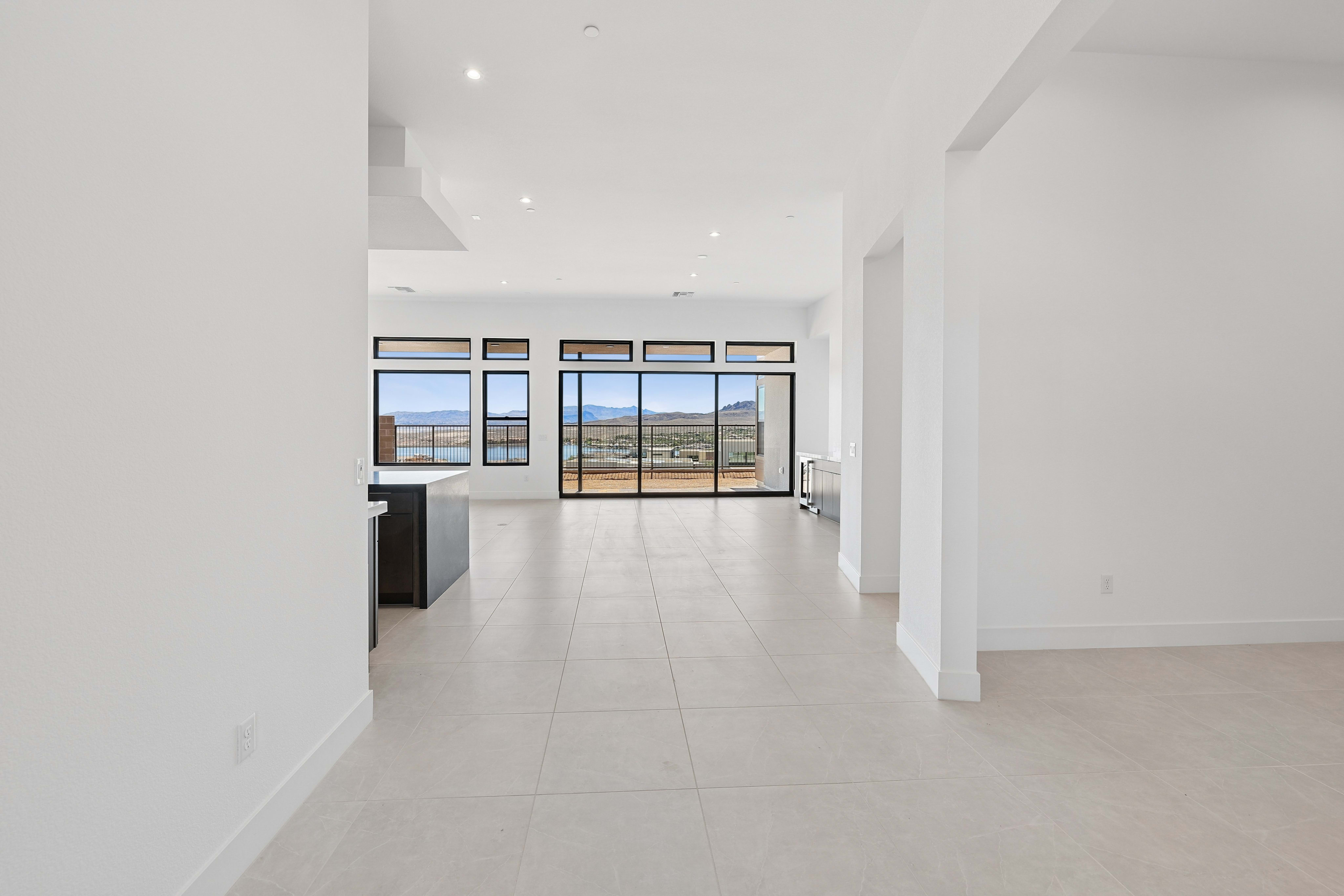 A modern, open-plan living space with a kitchen island in the foreground and expansive windows revealing a desert landscape in the background.