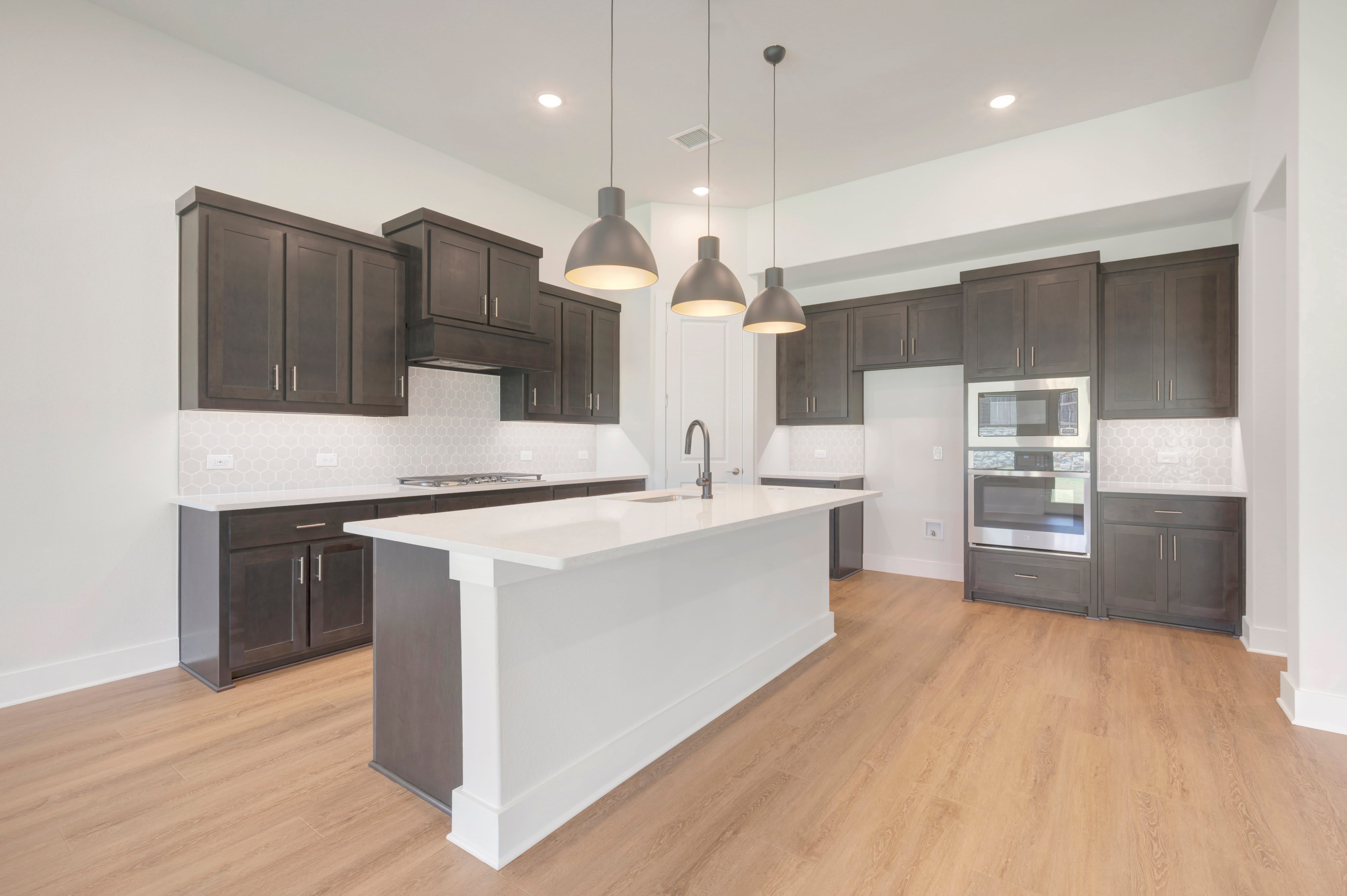 A modern kitchen with a white island in the foreground and dark cabinetry and appliances in the background.