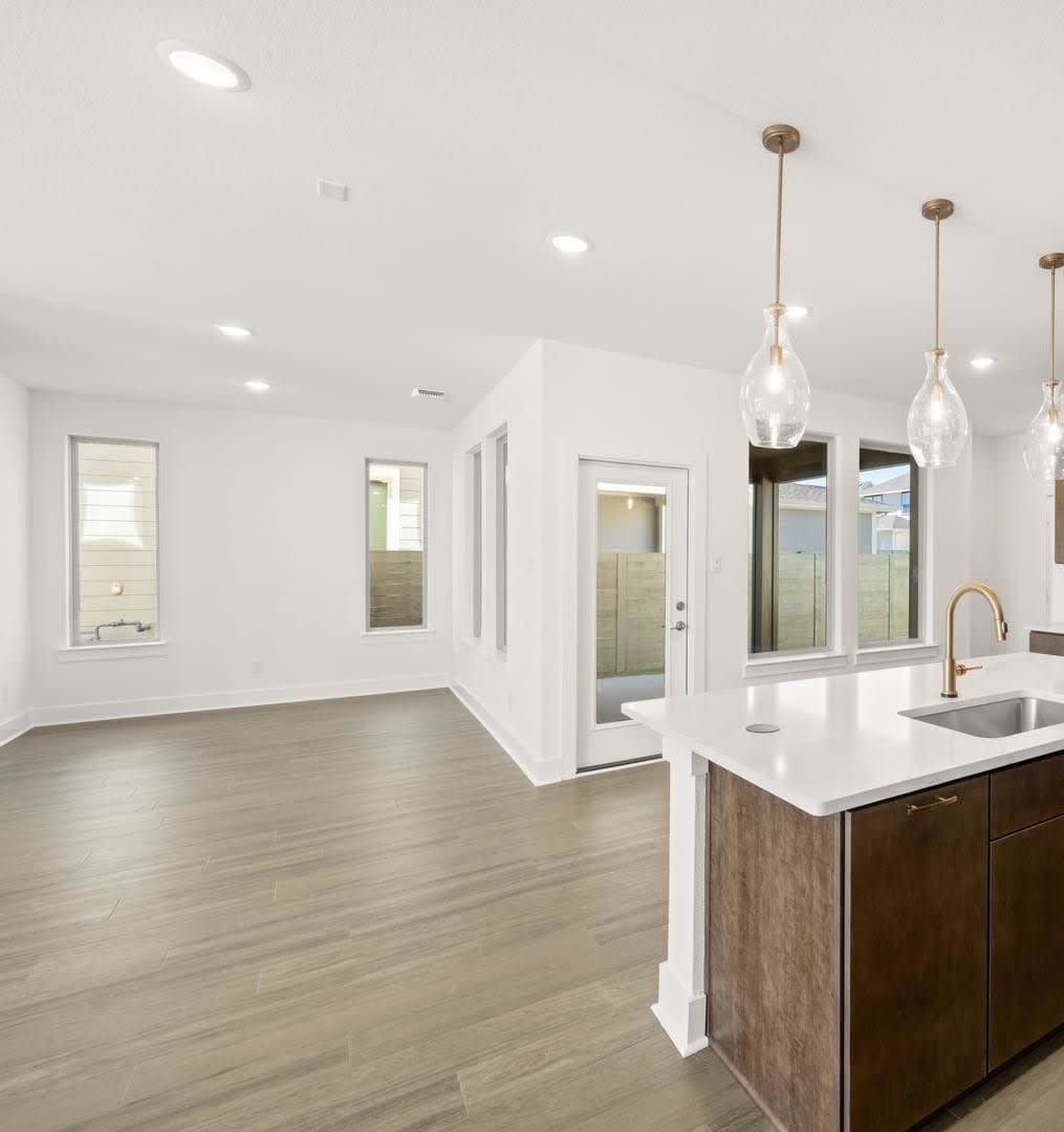 A modern, open-concept kitchen with a large island, wooden cabinets, and pendant lights, leading into a bright and airy living space with hardwood floors.