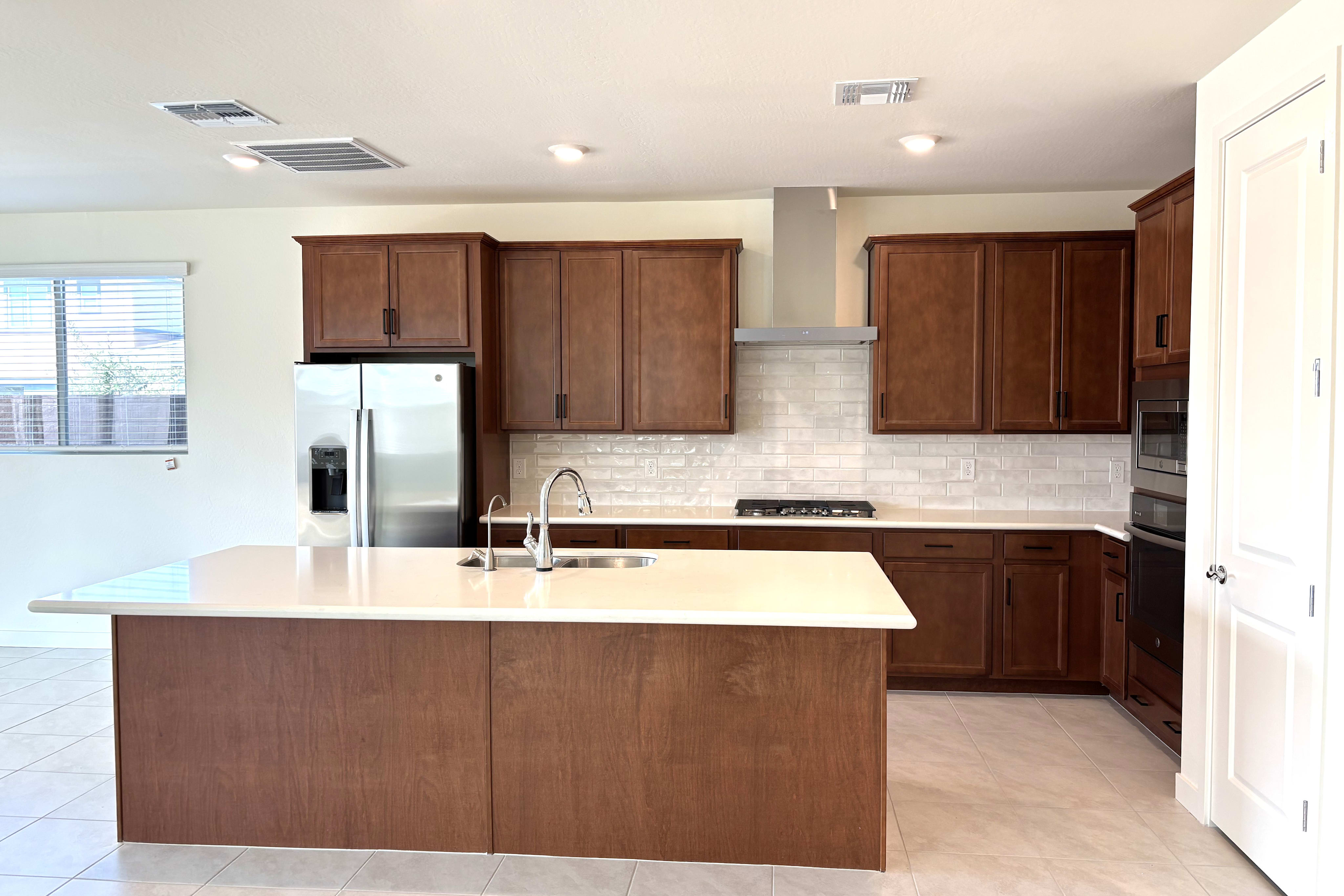 A modern kitchen with a large island in the foreground and stainless steel appliances and dark wood cabinets in the background.