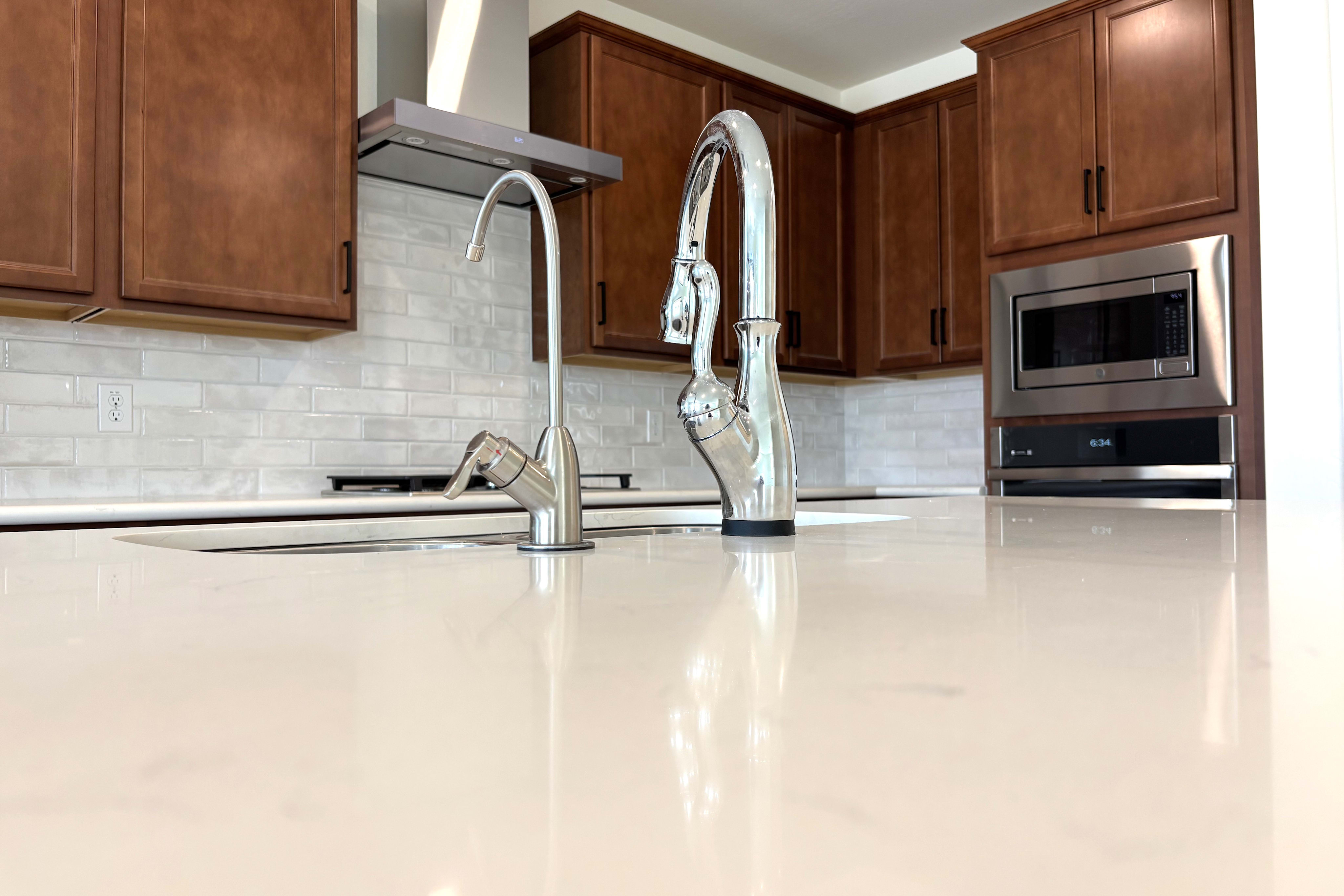 A bright white countertop in the foreground leads to a kitchen with dark wood cabinets, stainless steel appliances, and a white subway tile backsplash in the background.
