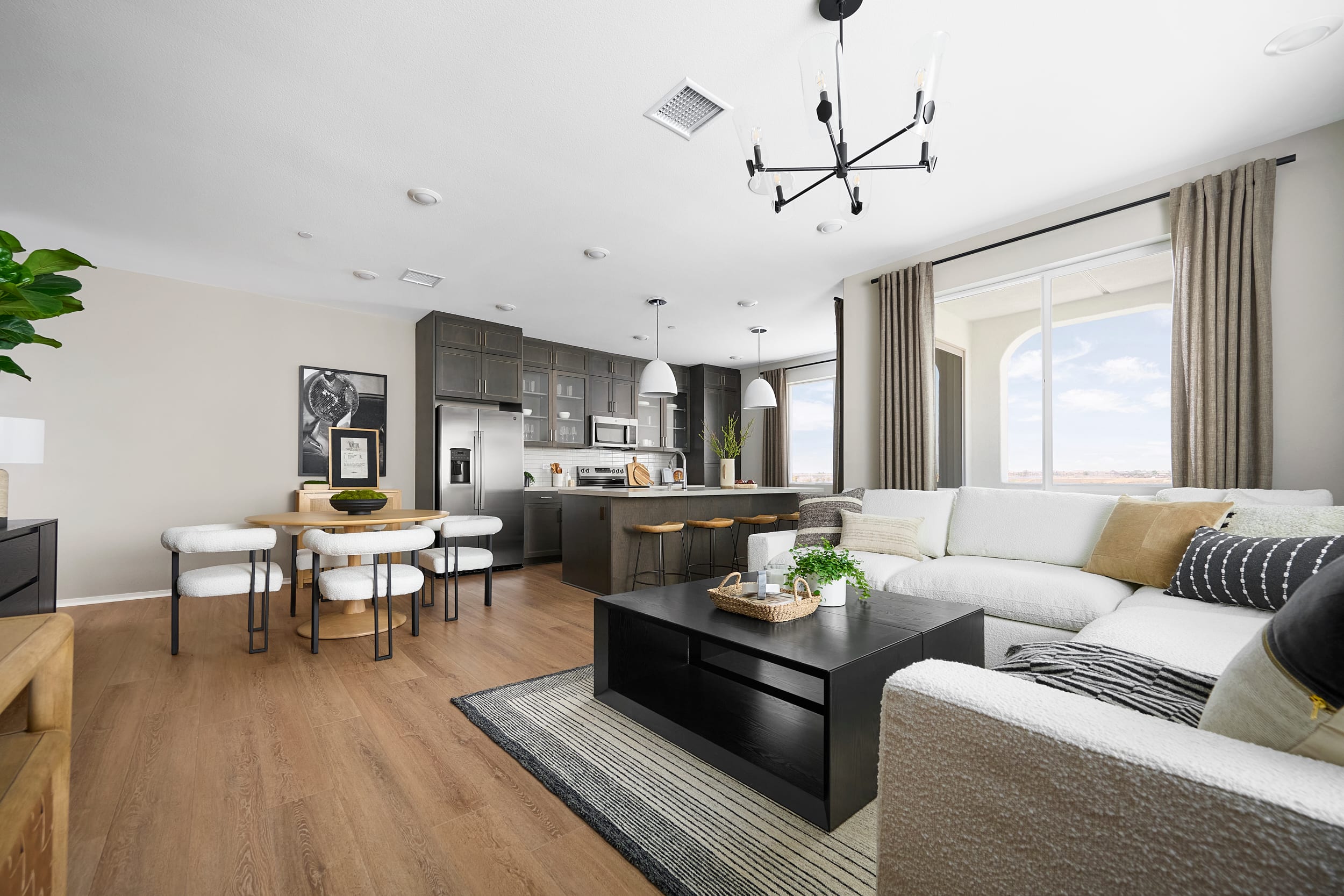 A modern living room with a sectional sofa and coffee table in the foreground, and a kitchen with an island and dining area in the background.
