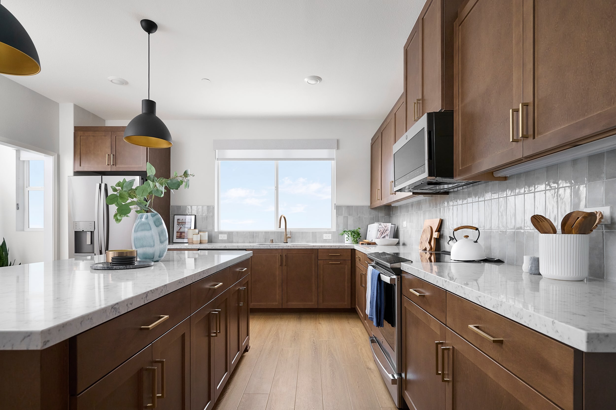 A modern kitchen with a white marble island in the foreground and wooden cabinets and a large window with a view of the sky in the background.