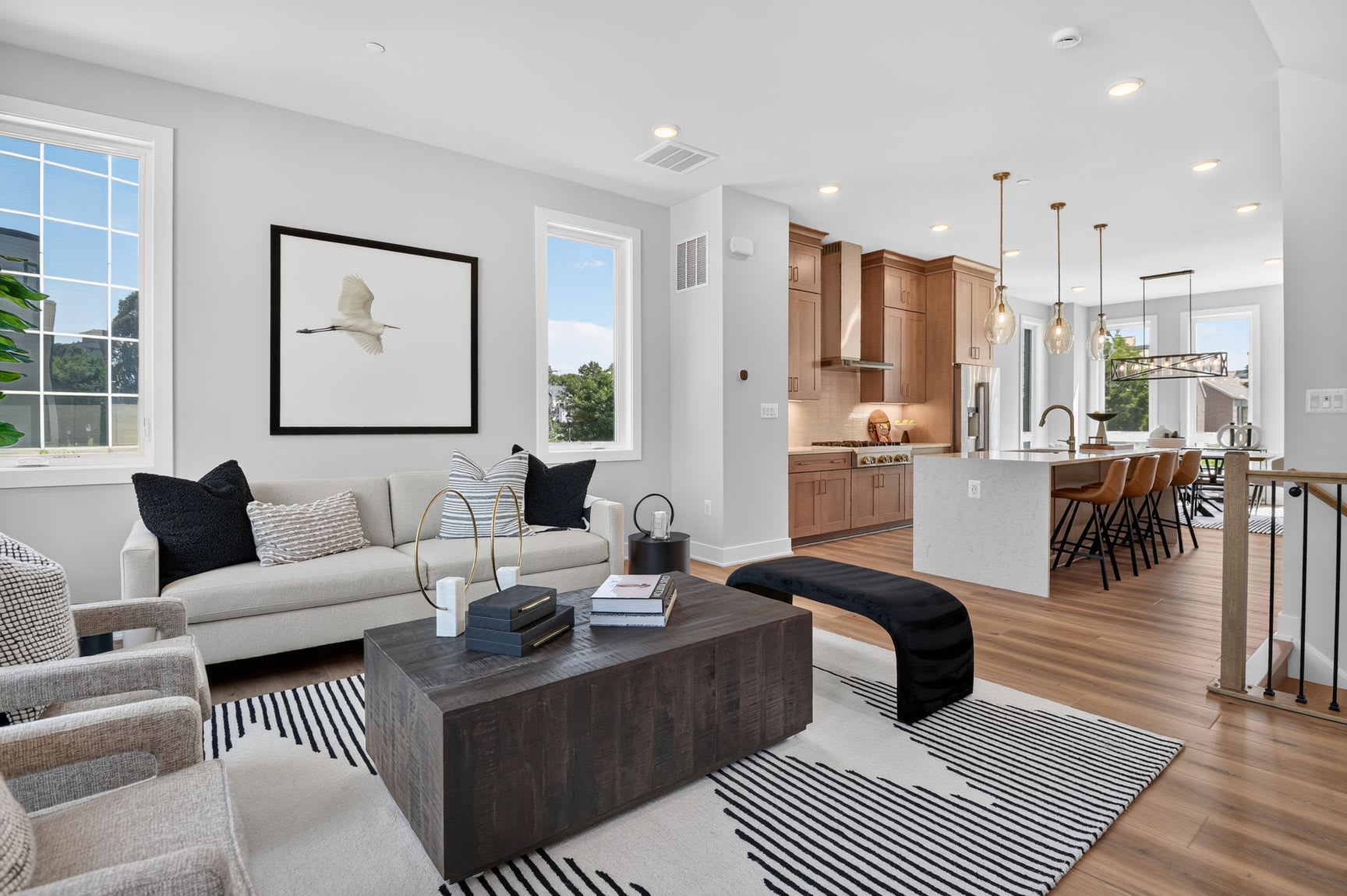 A modern living room with a large sectional sofa and coffee table in the foreground opens to a kitchen with a breakfast bar and island in the background.