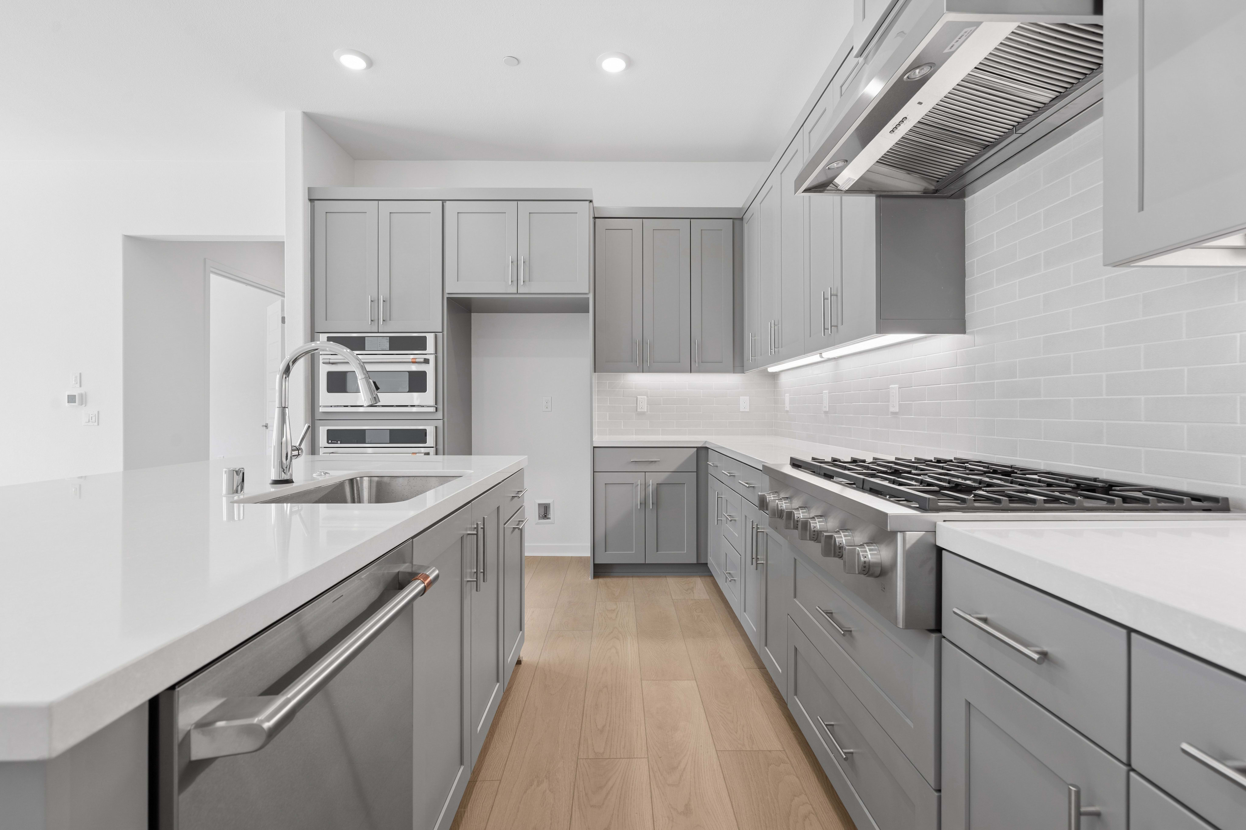 A modern gray kitchen with a white countertop island in the foreground and stainless steel appliances and white subway tile backsplash in the background.