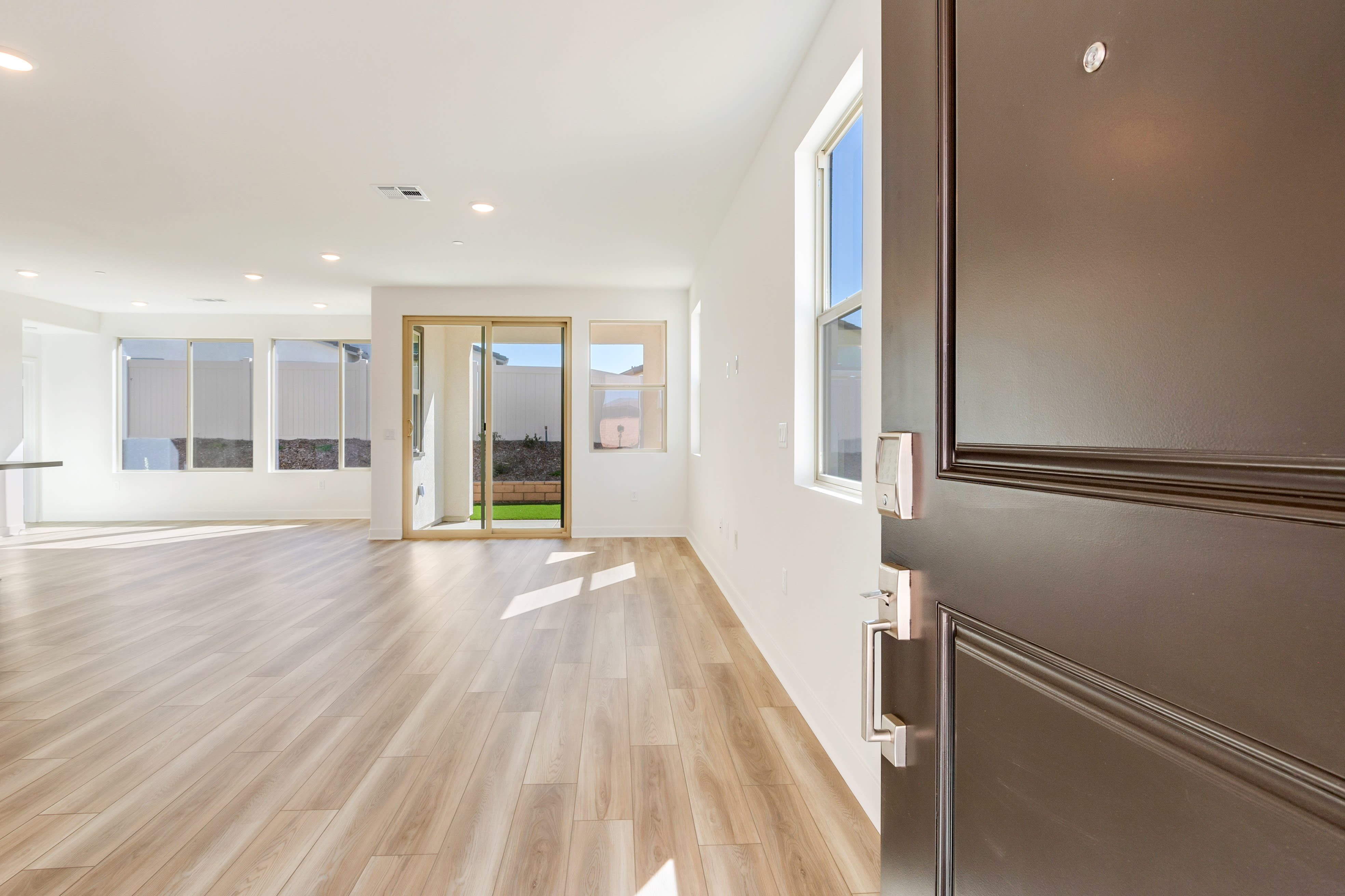 A dark gray front door opens into a bright, empty living room with large windows and a view of a backyard.