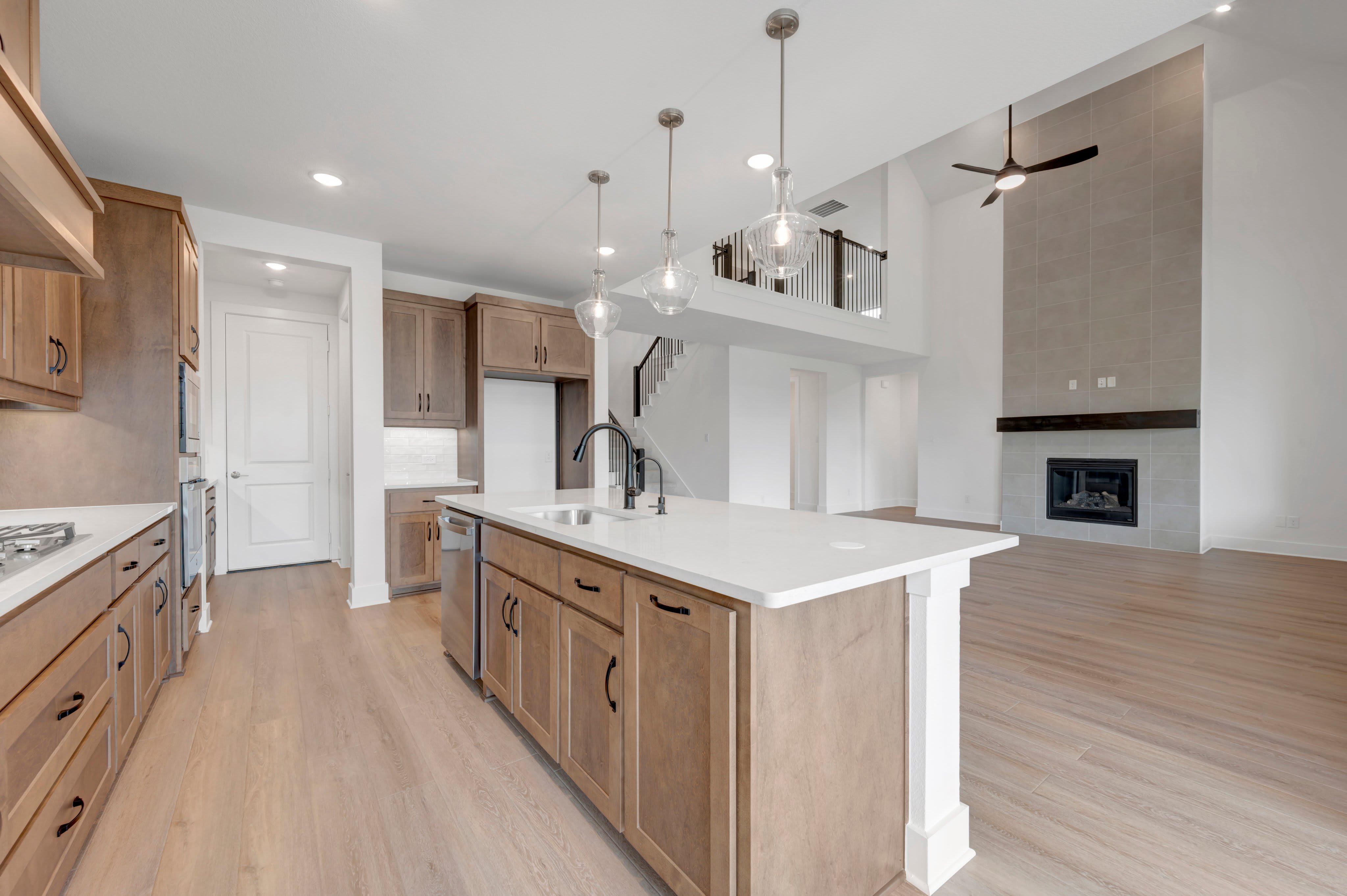 A modern kitchen island with a sink and pendant lights is in the foreground, while a spacious living area with a fireplace and high ceilings is in the background.