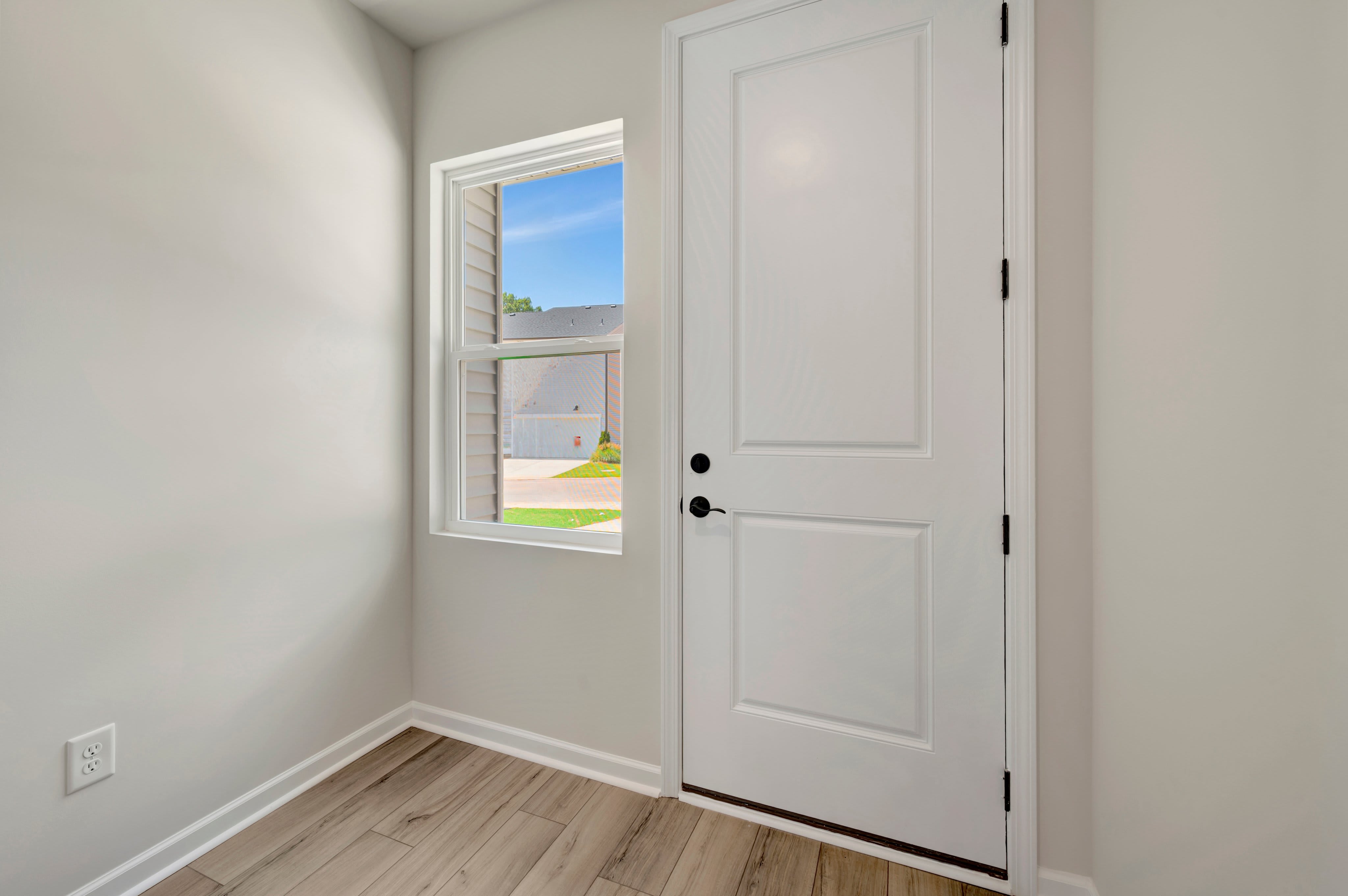 A white door and a window with a view of a sunny street are in the foreground, while a neutral-colored wall and floor fill the background.