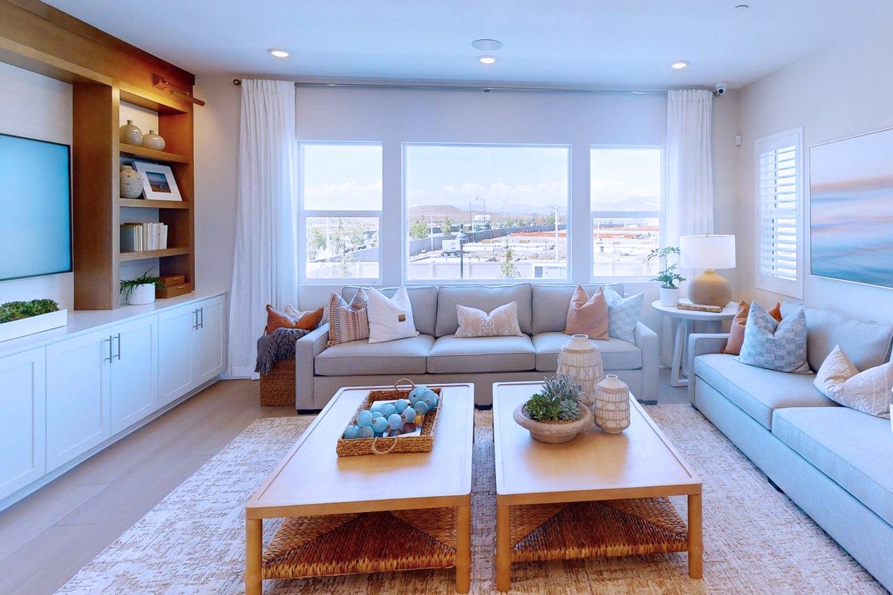 Two light blue sofas face a large window with a desert landscape view, while two wooden coffee tables with decorative items sit on a patterned rug in the foreground.