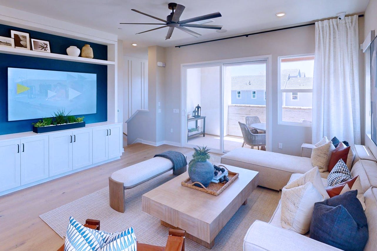 A modern living room with a large sectional sofa and coffee table in the foreground, and a sliding glass door leading to an outdoor patio in the background.