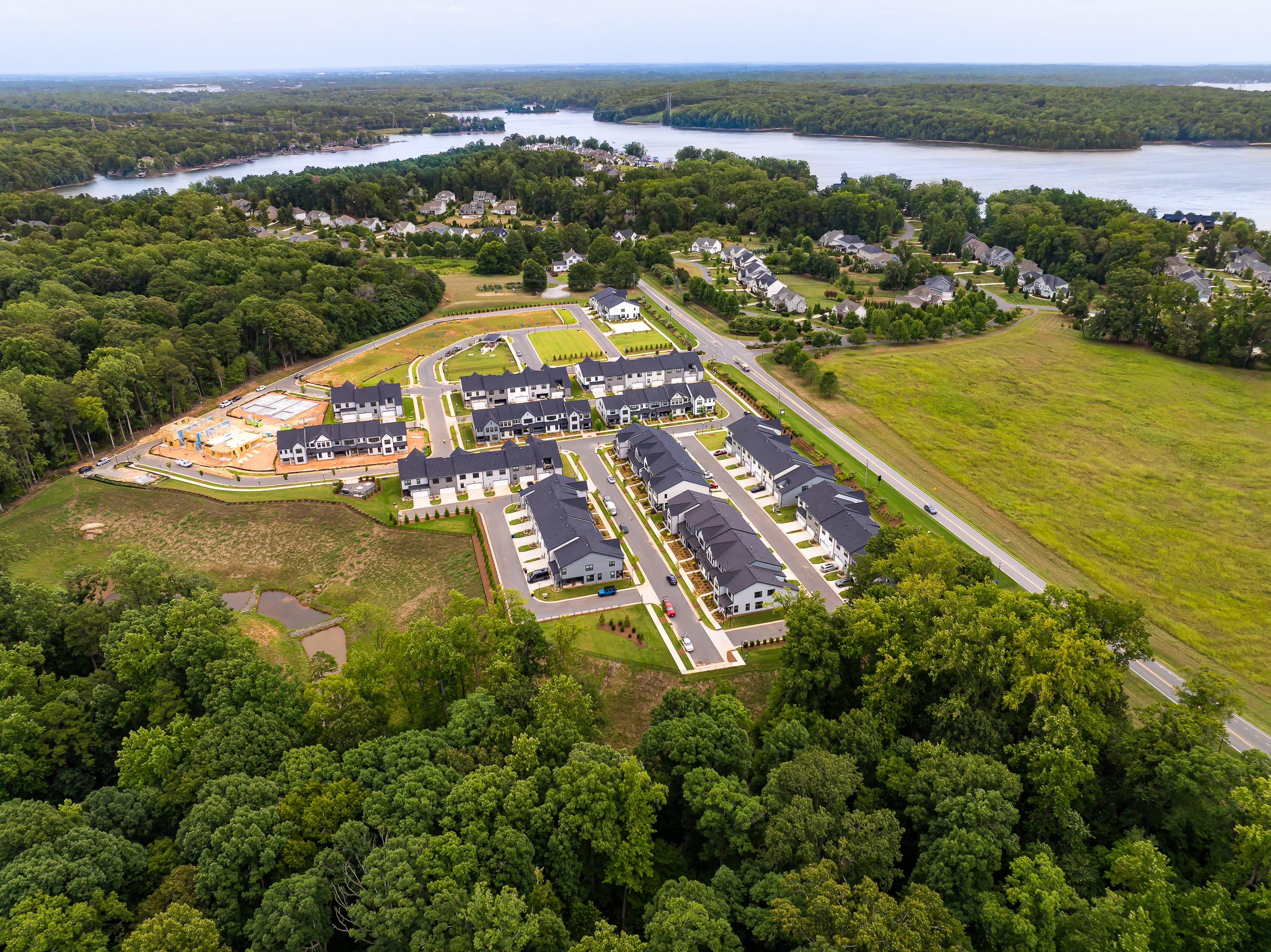 A new housing development with rows of townhouses sits on a hill overlooking a wide river and surrounding green landscape.