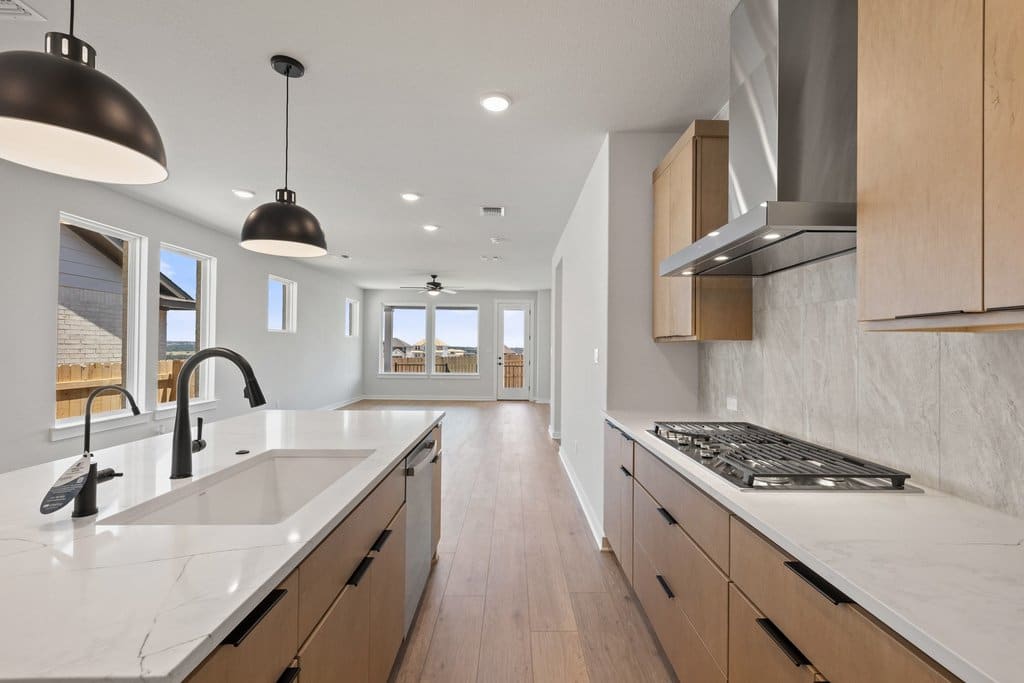 A modern kitchen with a white countertop island in the foreground opens to a spacious living area with large windows in the background.