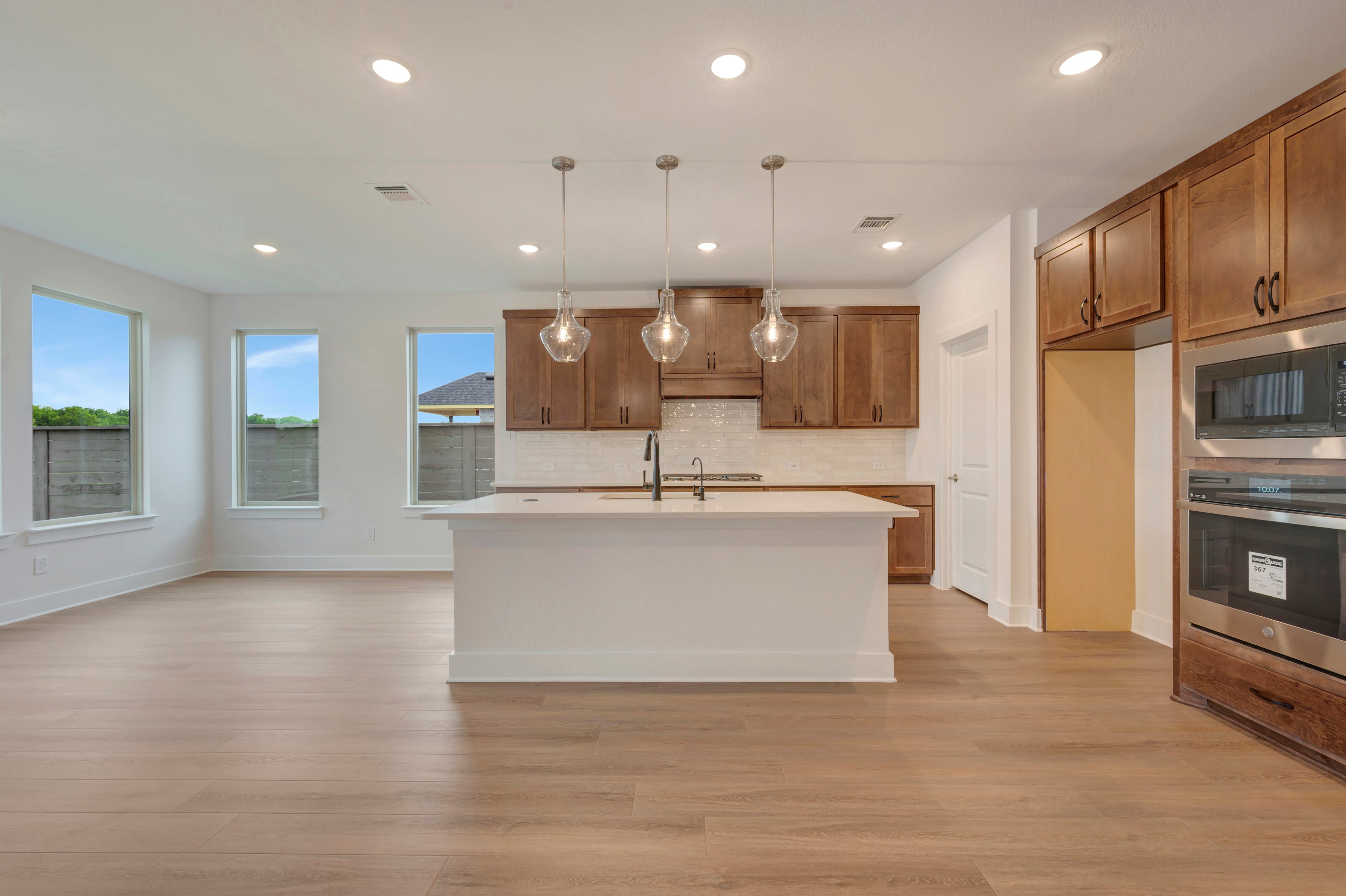 A modern kitchen with a white island in the foreground and wooden cabinets and stainless steel appliances in the background.
