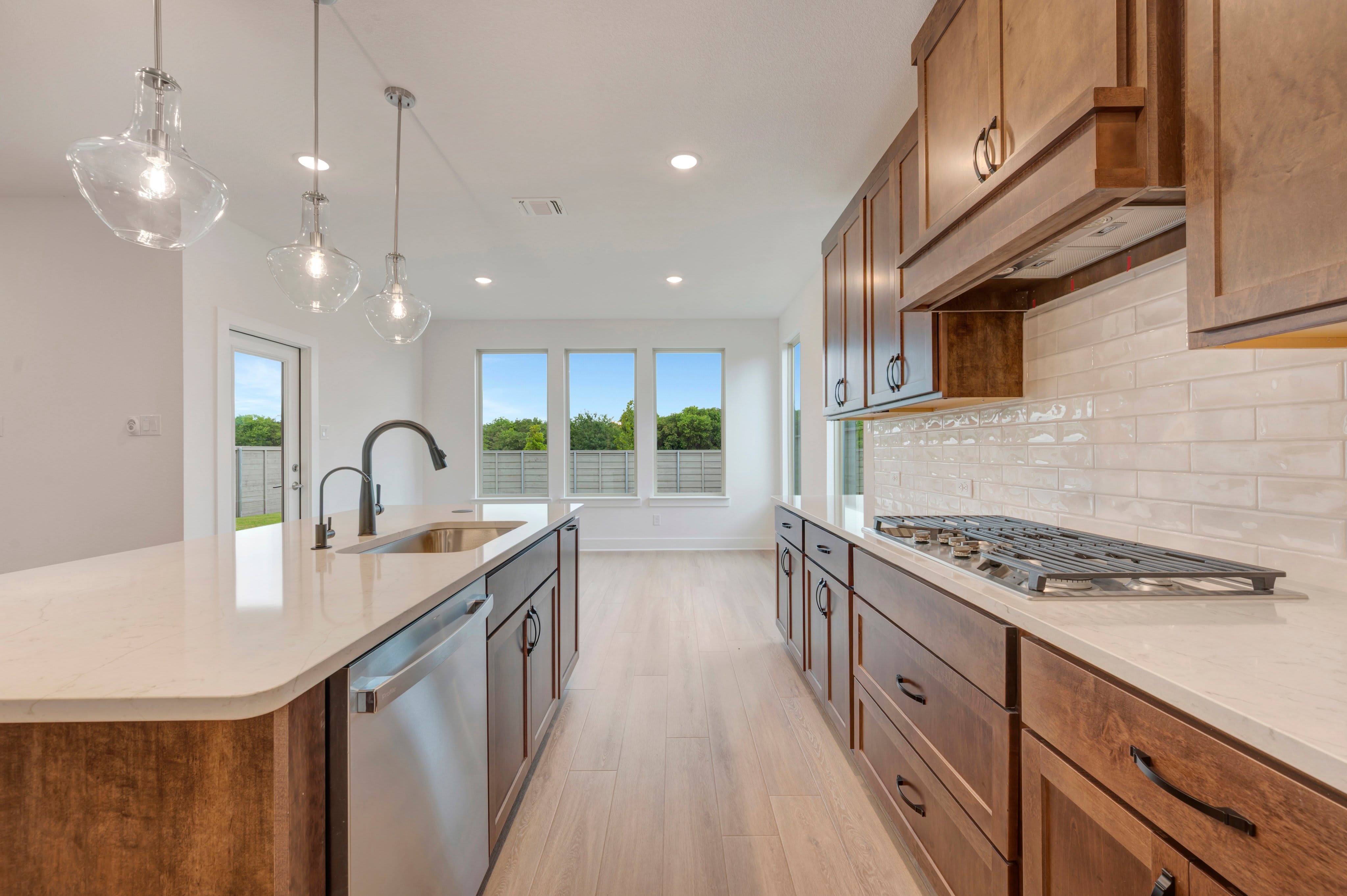 A modern kitchen with a large island in the foreground and a dining area with a view of greenery in the background.