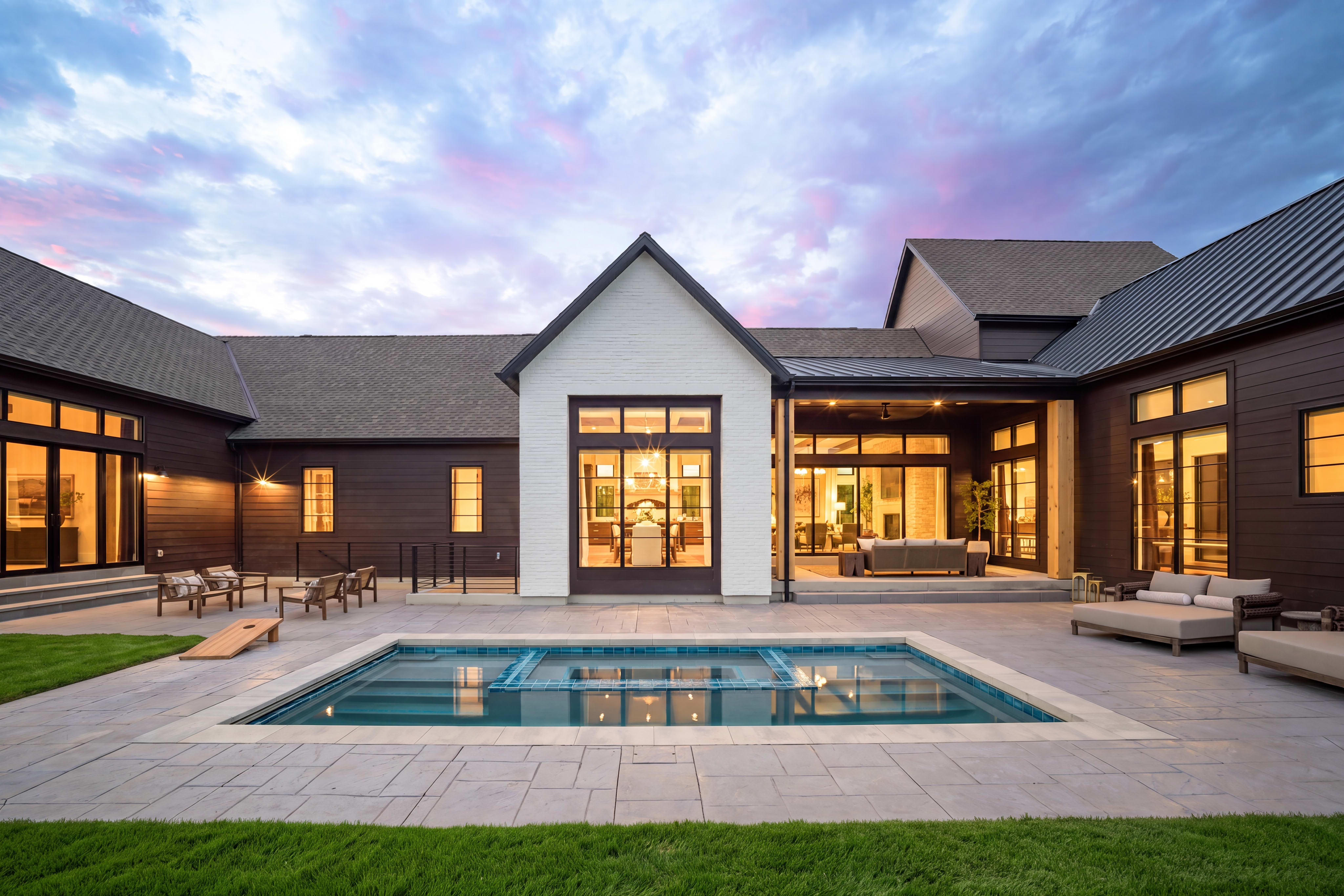 A modern home with a swimming pool in the foreground is set against a twilight sky.