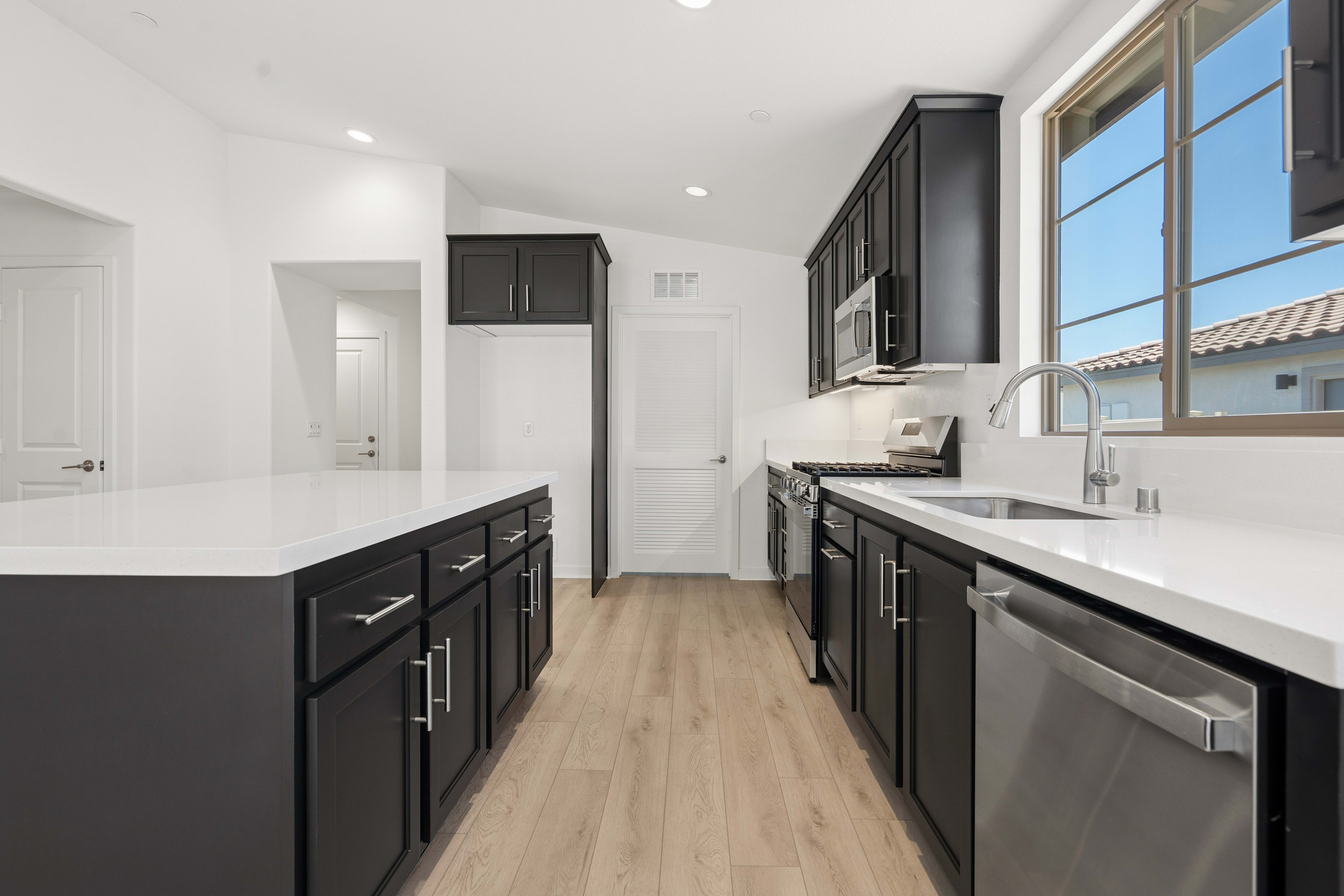 A modern kitchen with a dark island in the foreground and a window overlooking a sunny neighborhood in the background.