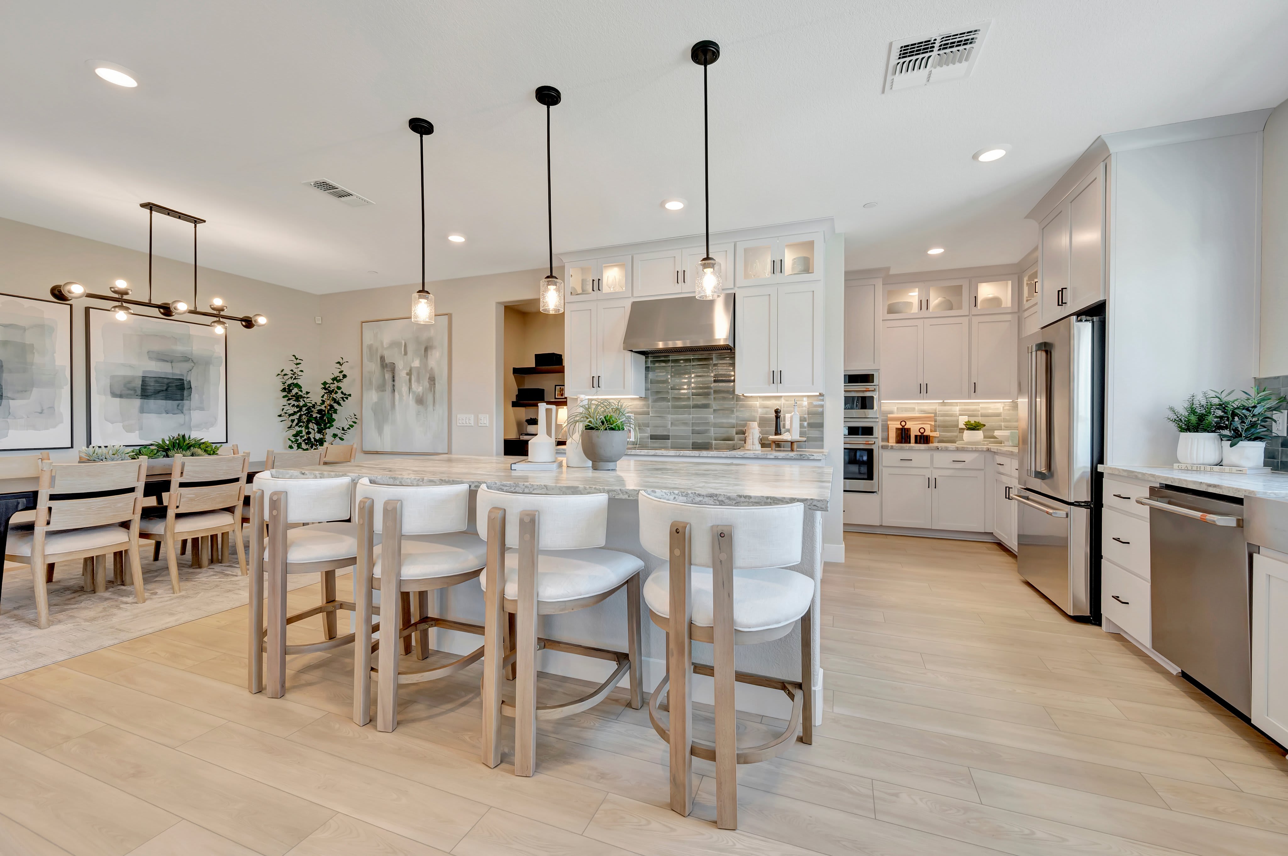 A modern kitchen with a large island and bar stools in the foreground, and a dining area with a table and chairs in the background.