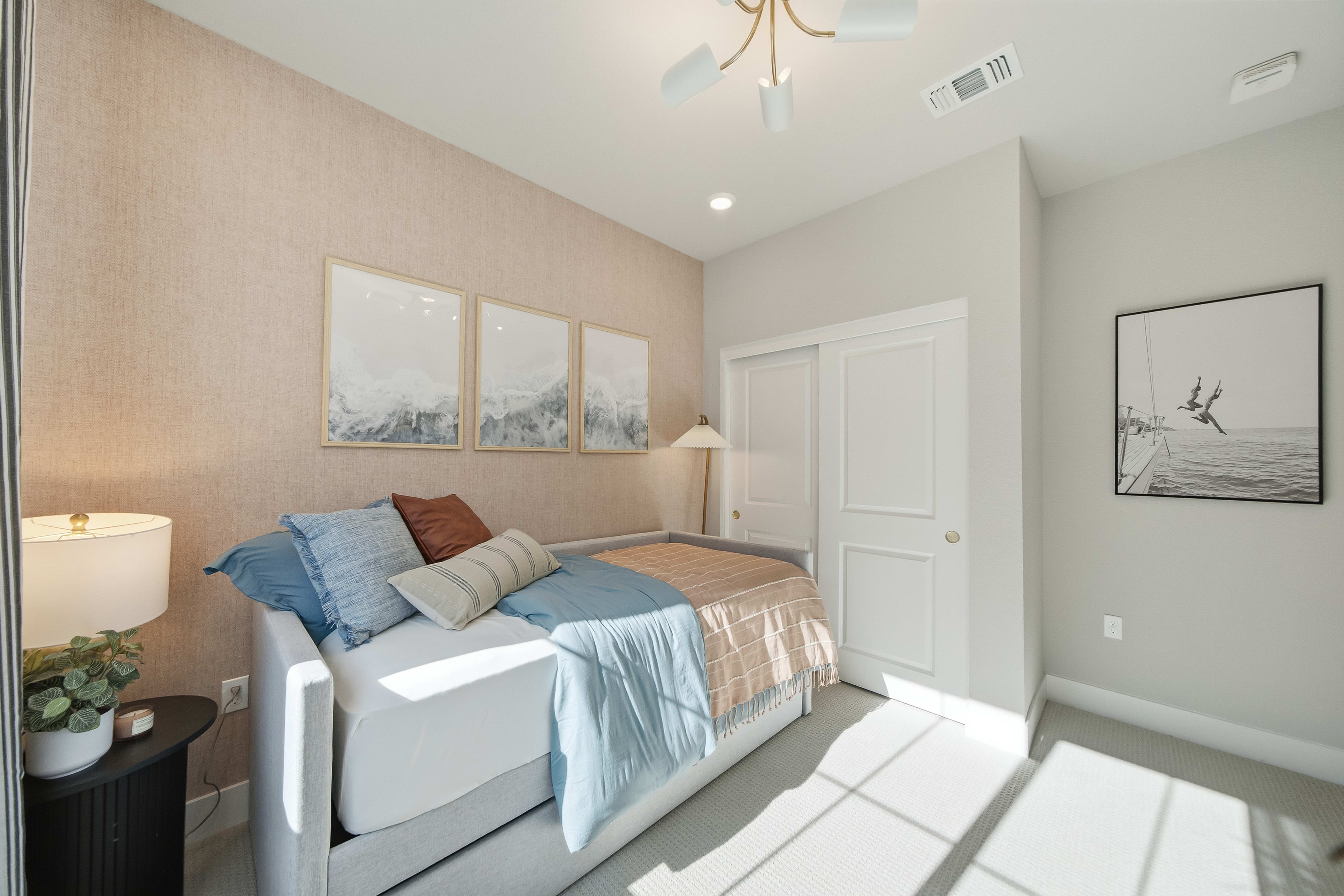A daybed with blue and brown bedding is in the foreground, while a closet and artwork adorn the background.