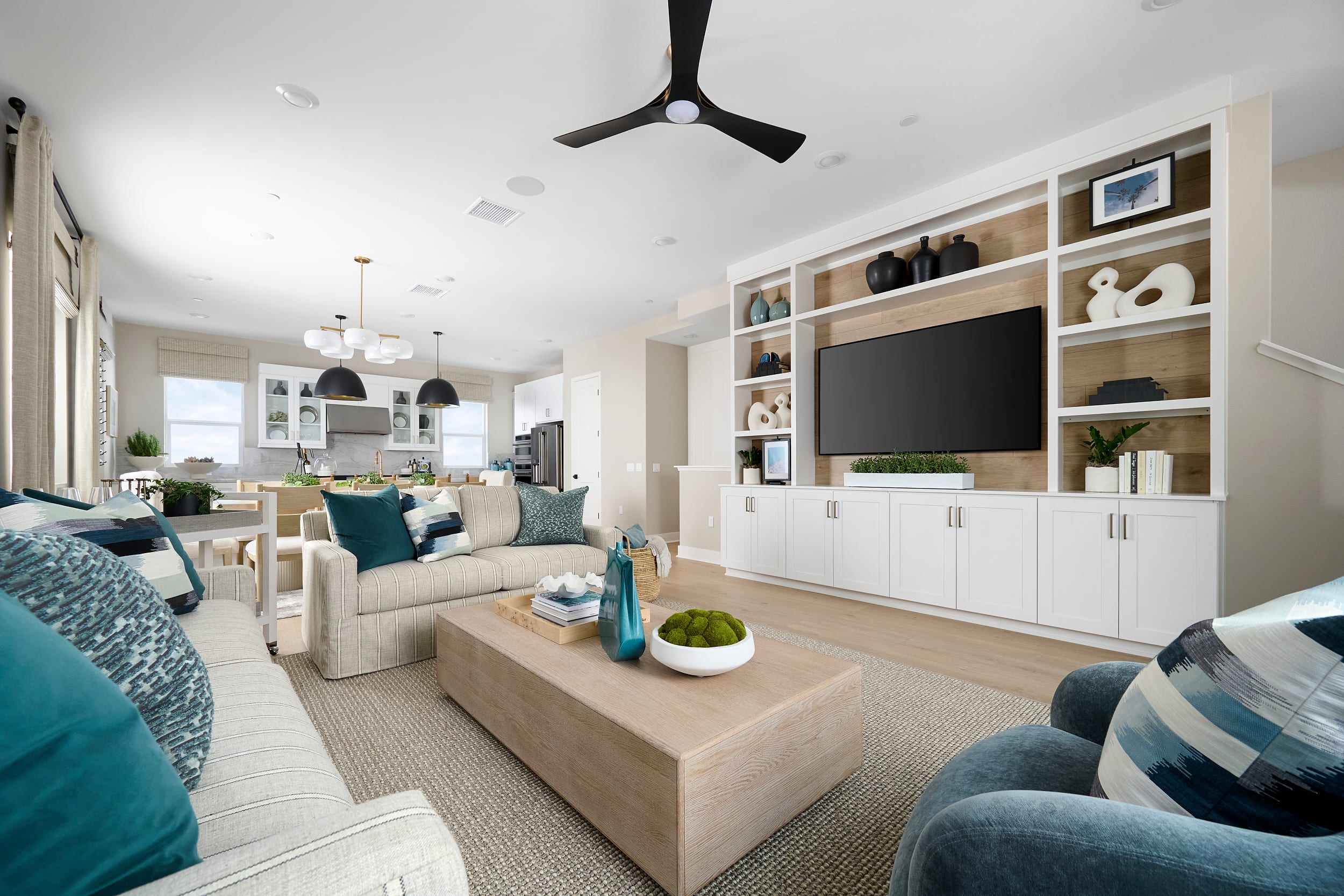 A modern living room with a large sectional sofa and coffee table in the foreground, and a spacious open-plan kitchen and dining area in the background.