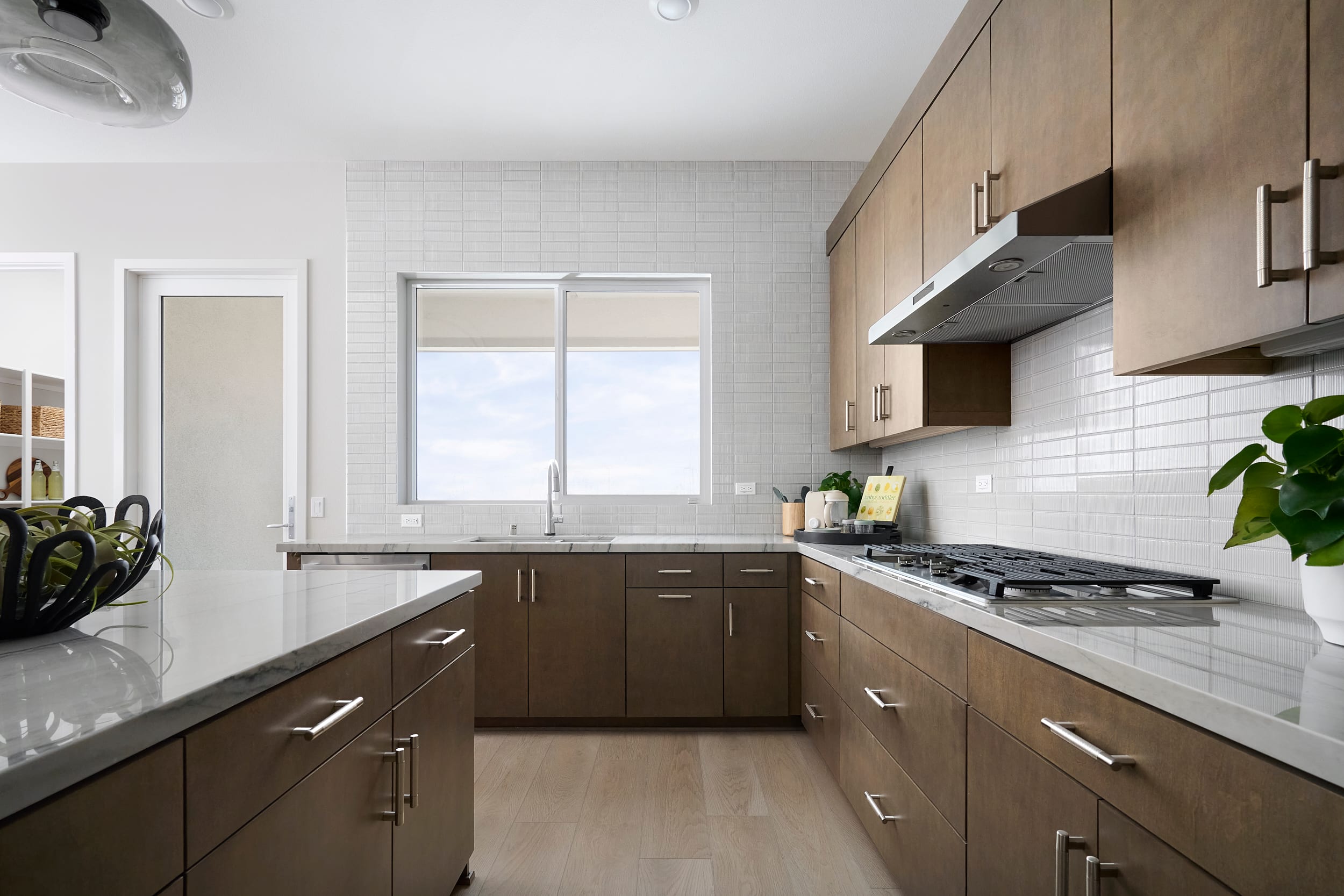 A modern kitchen with a marble island in the foreground and a window overlooking a bright sky in the background.