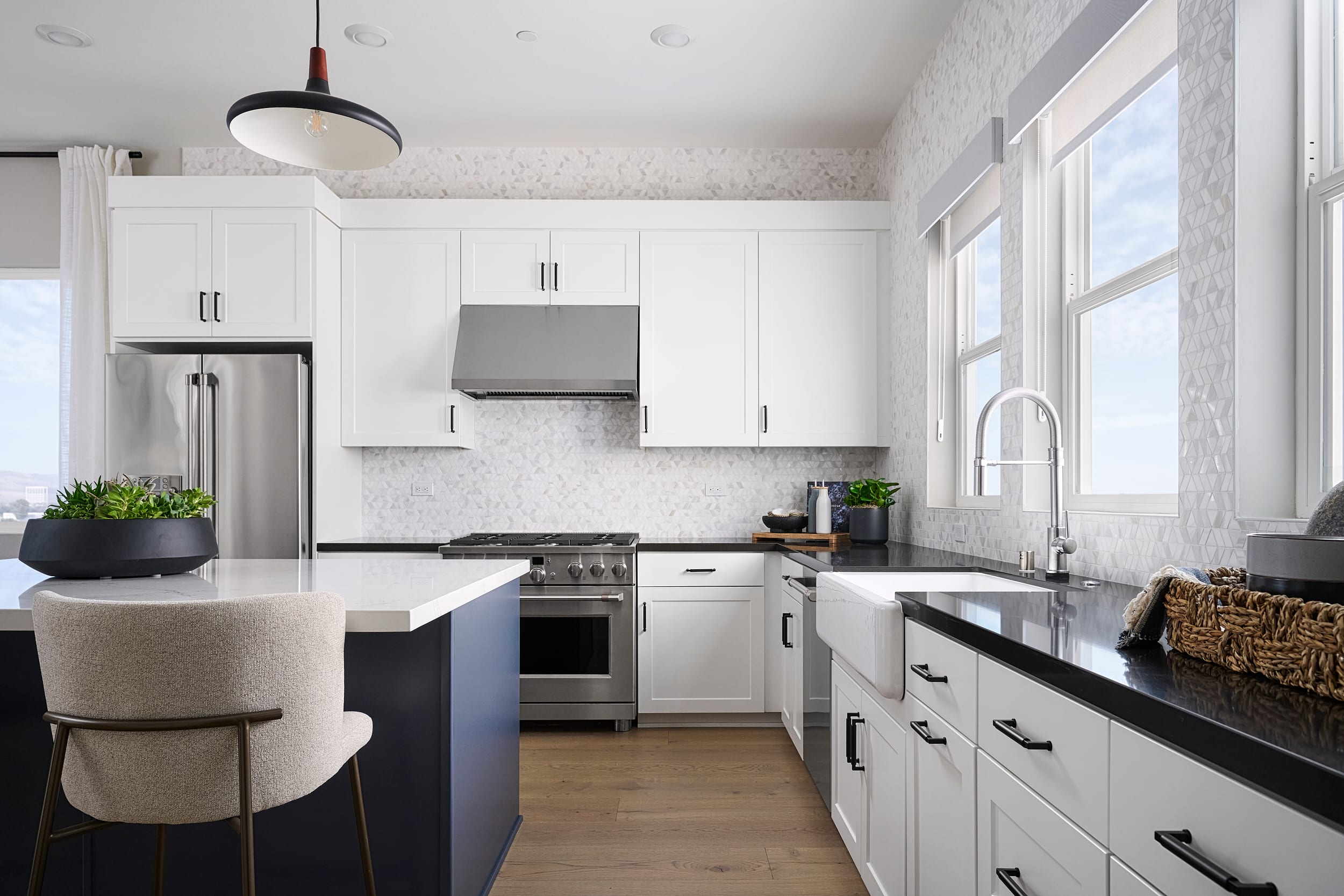 A modern kitchen with a dark blue island and white cabinets in the foreground, and a stainless steel range and white tiled backsplash in the background.
