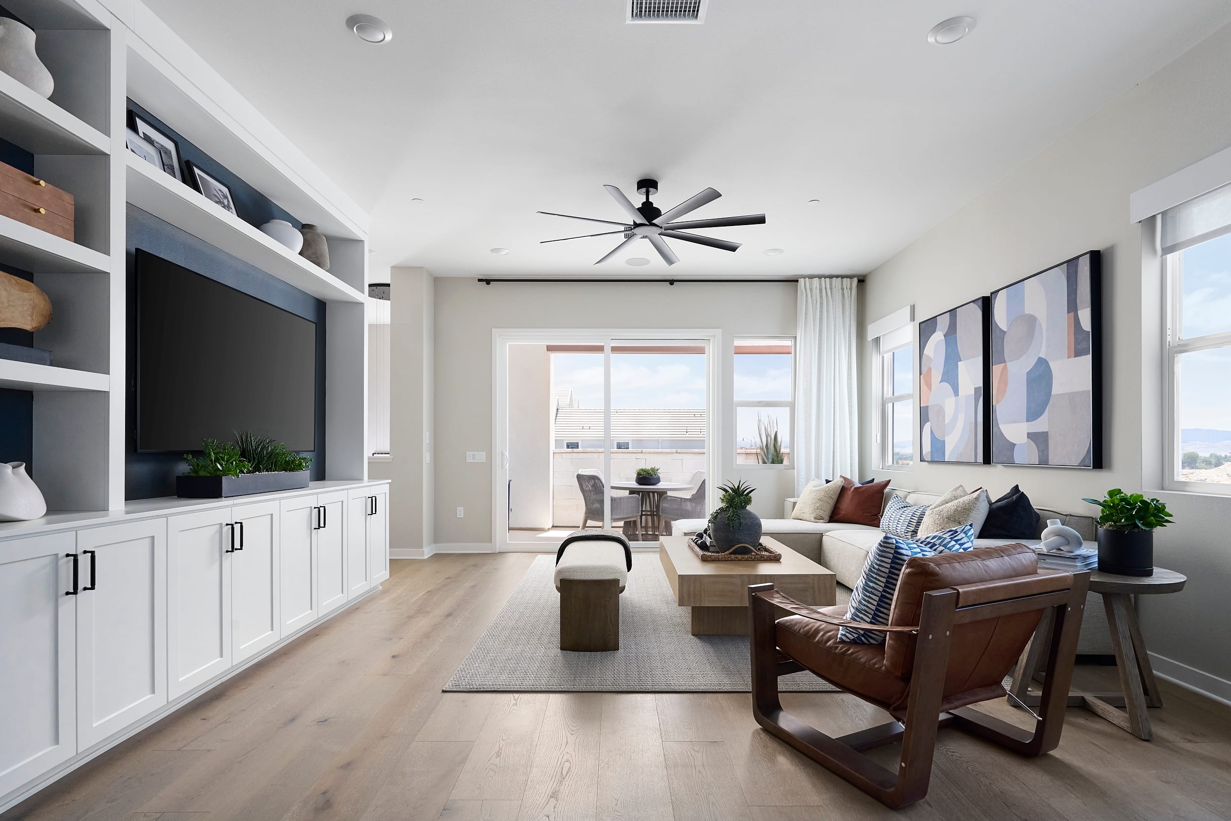 A modern living room with a built-in entertainment center on the left and a large sectional sofa facing a sliding glass door leading to a patio in the background.
