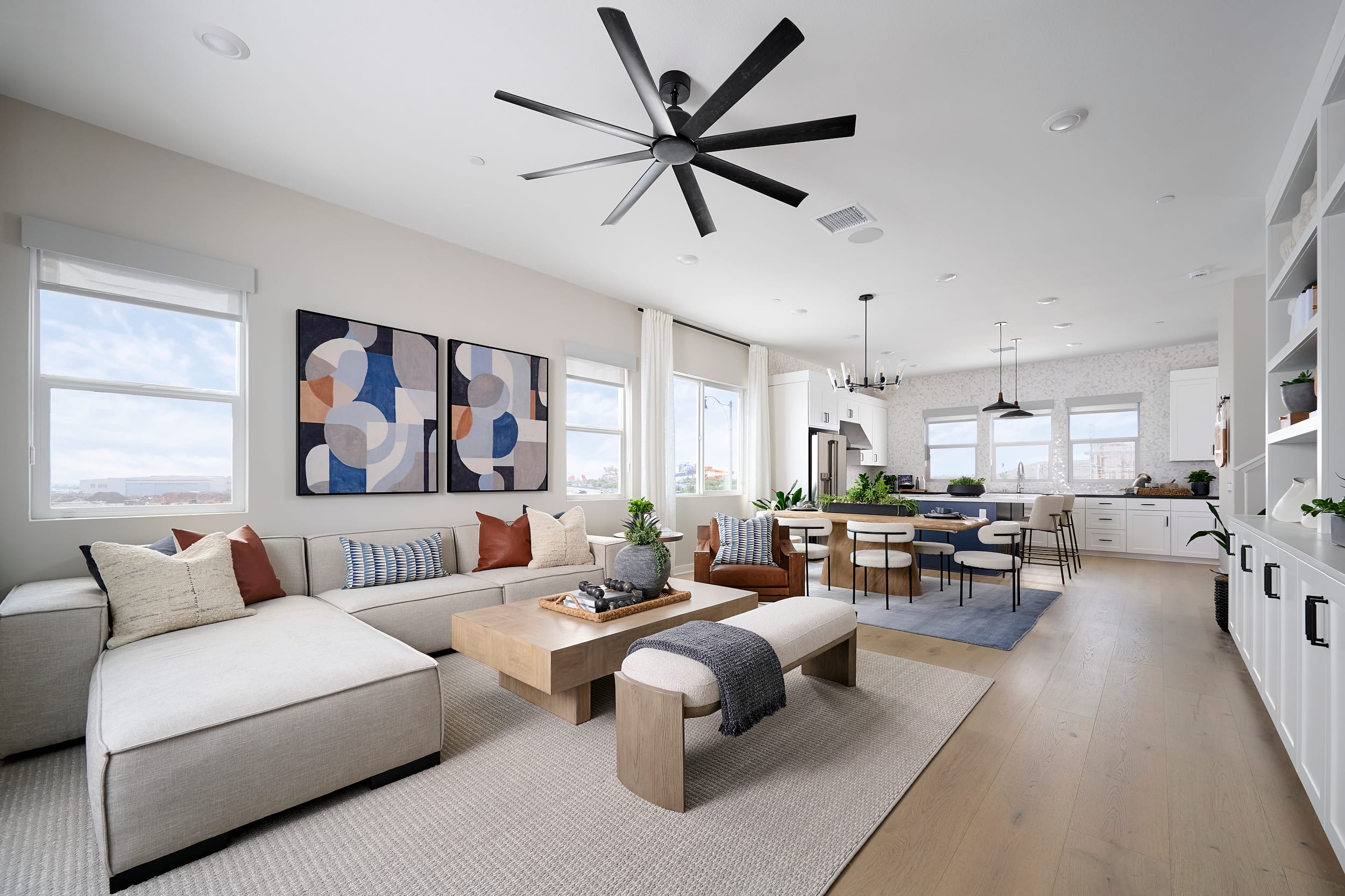 A modern living room with a sectional sofa and coffee table in the foreground transitions into a dining area and kitchen in the background.