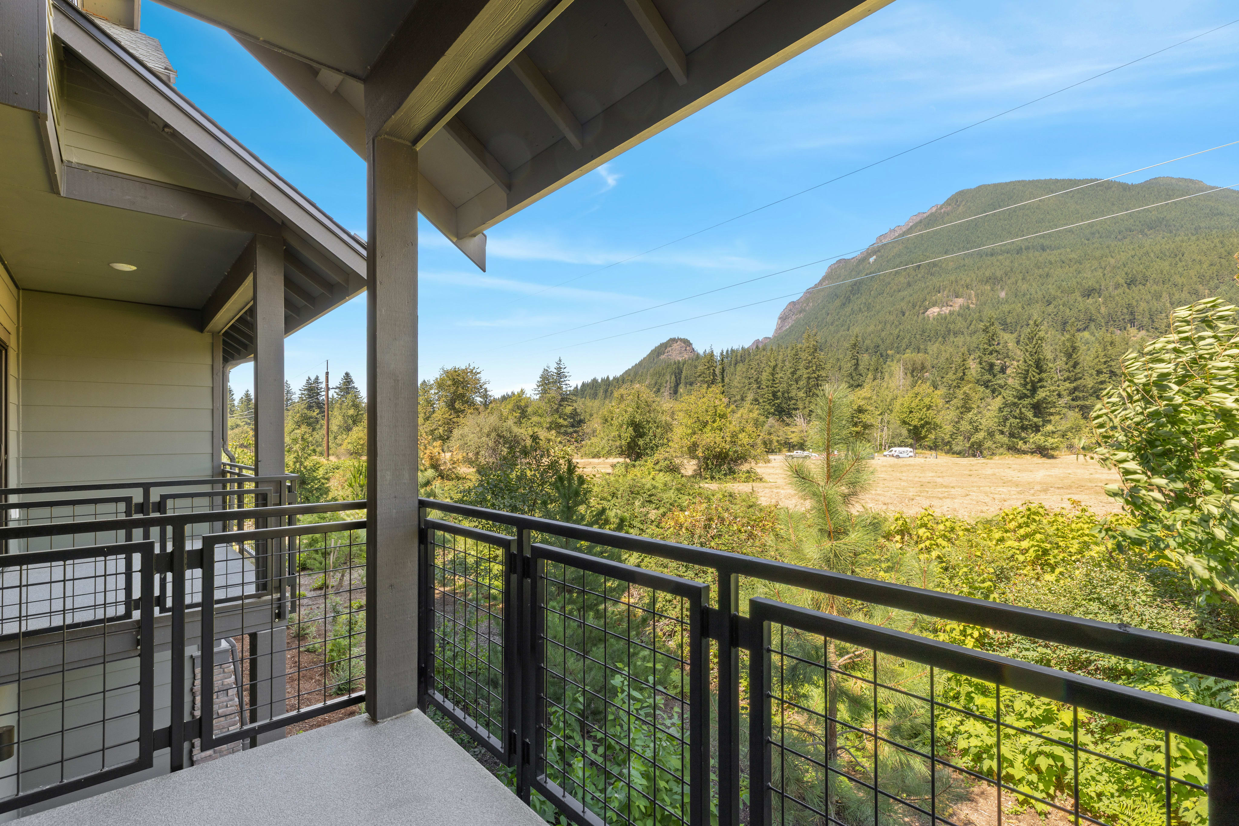 A modern balcony with metal railings overlooks a lush green landscape with a large mountain in the background.