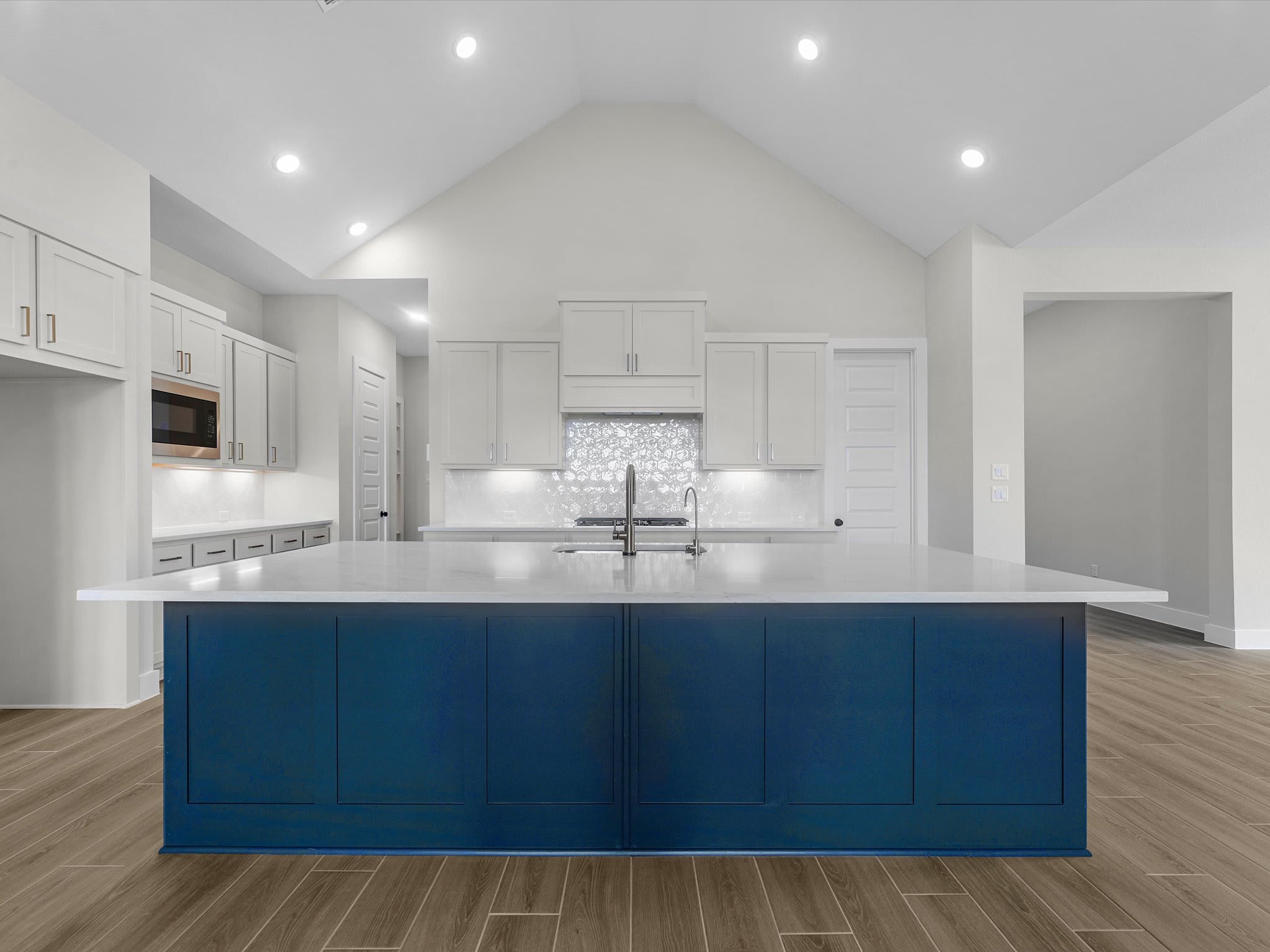A spacious, modern kitchen features a large blue island in the foreground and white cabinetry with stainless steel appliances in the background.