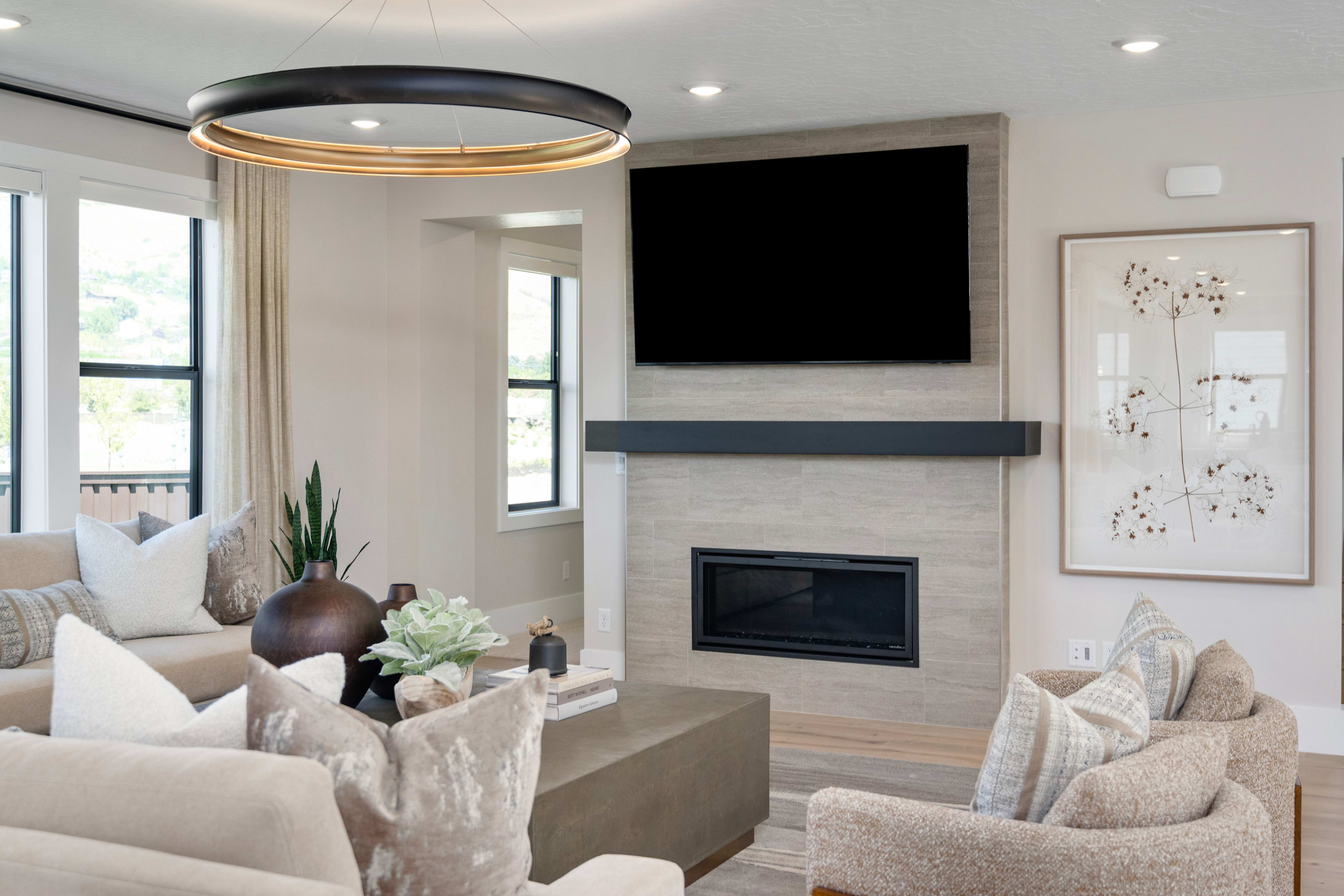 A modern living room features a large sectional sofa and armchair in the foreground, with a fireplace and mounted television in the background.