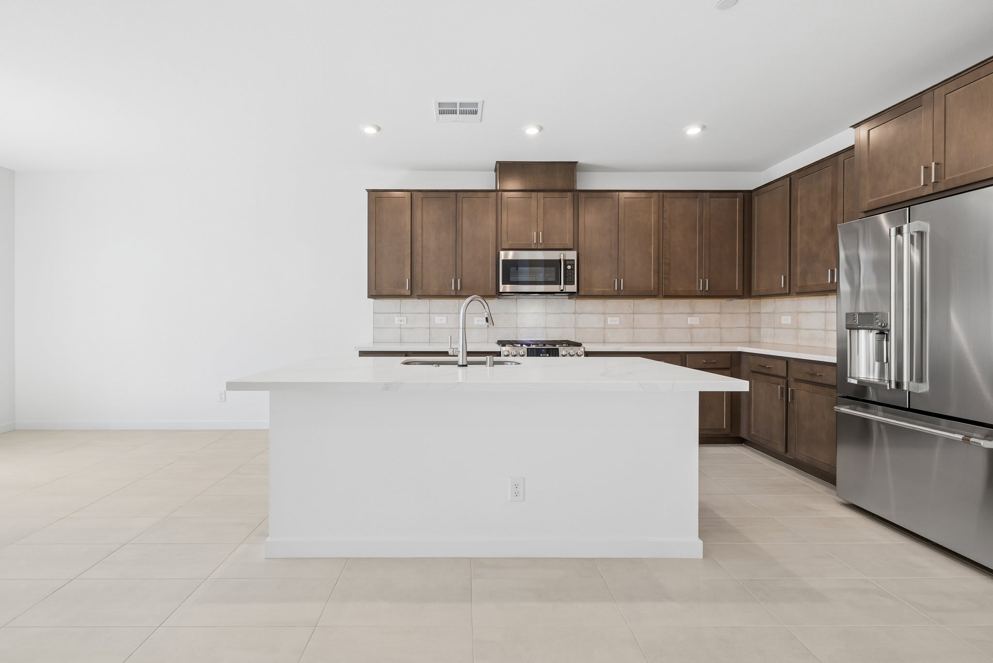 A modern kitchen with a white island in the foreground and dark wood cabinets and stainless steel appliances in the background.