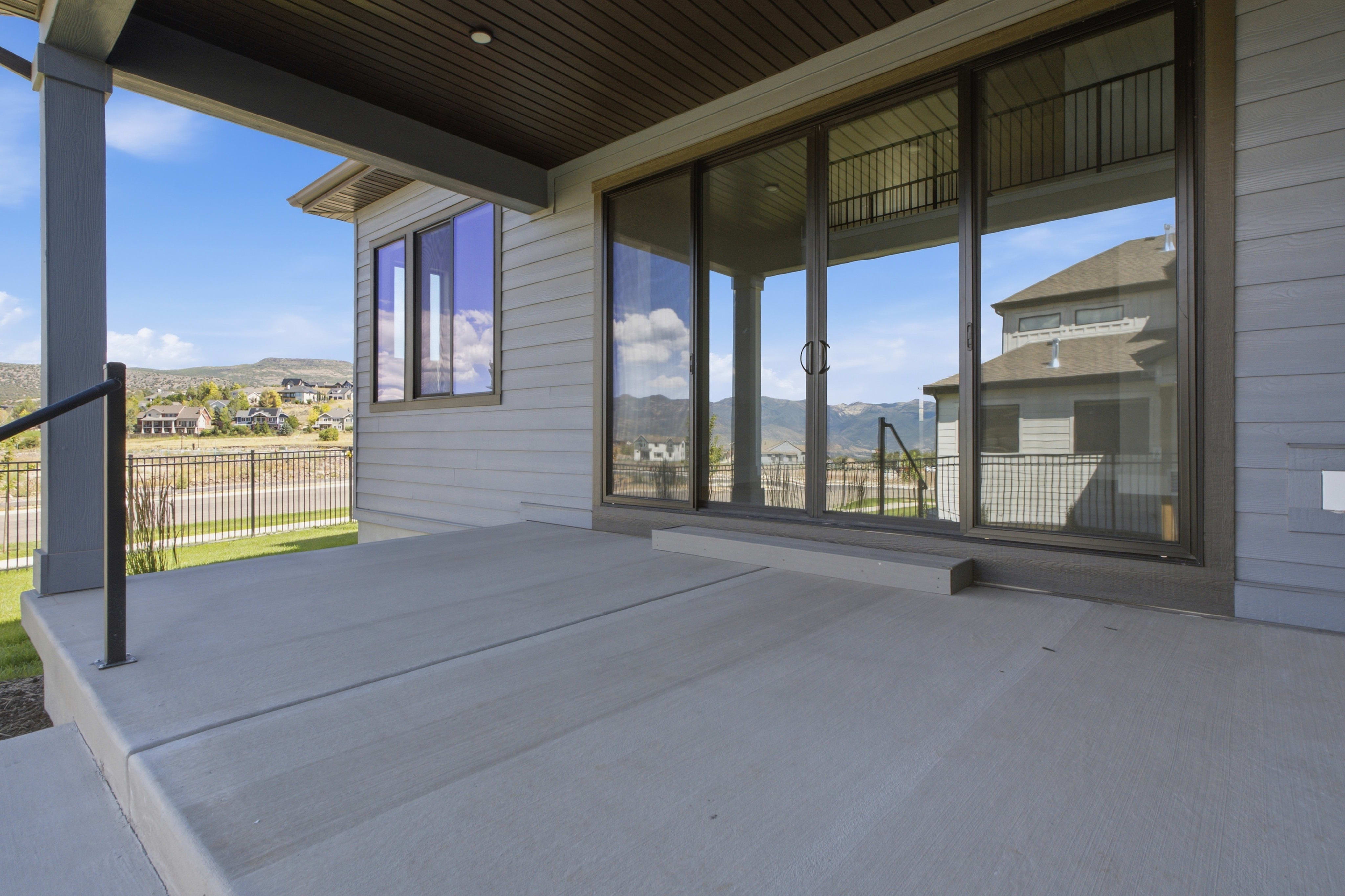A concrete patio with large sliding glass doors leads to a view of houses and hills under a blue sky.