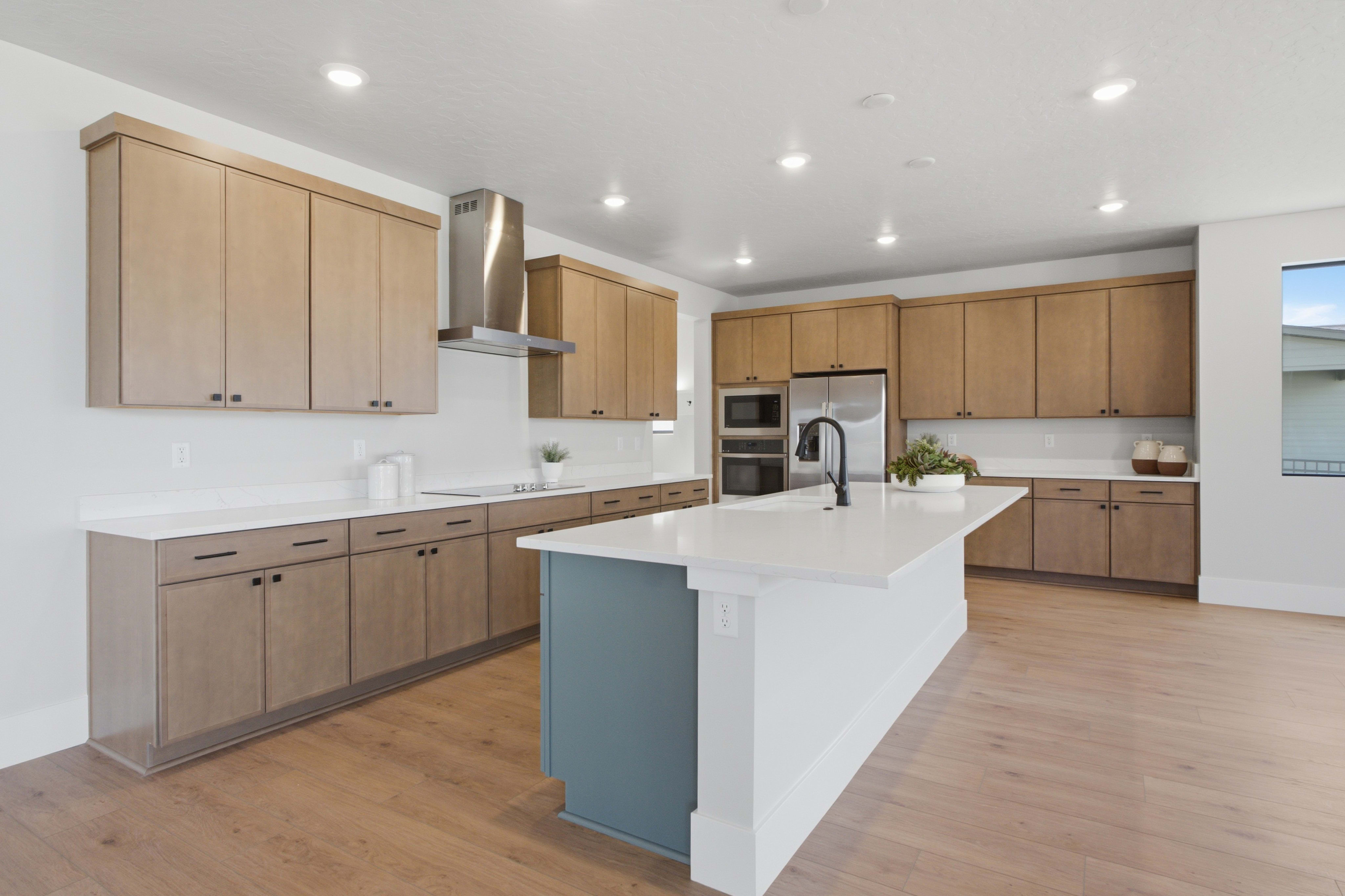 A modern kitchen with a blue-accented island in the foreground and light wood cabinetry and stainless steel appliances in the background.