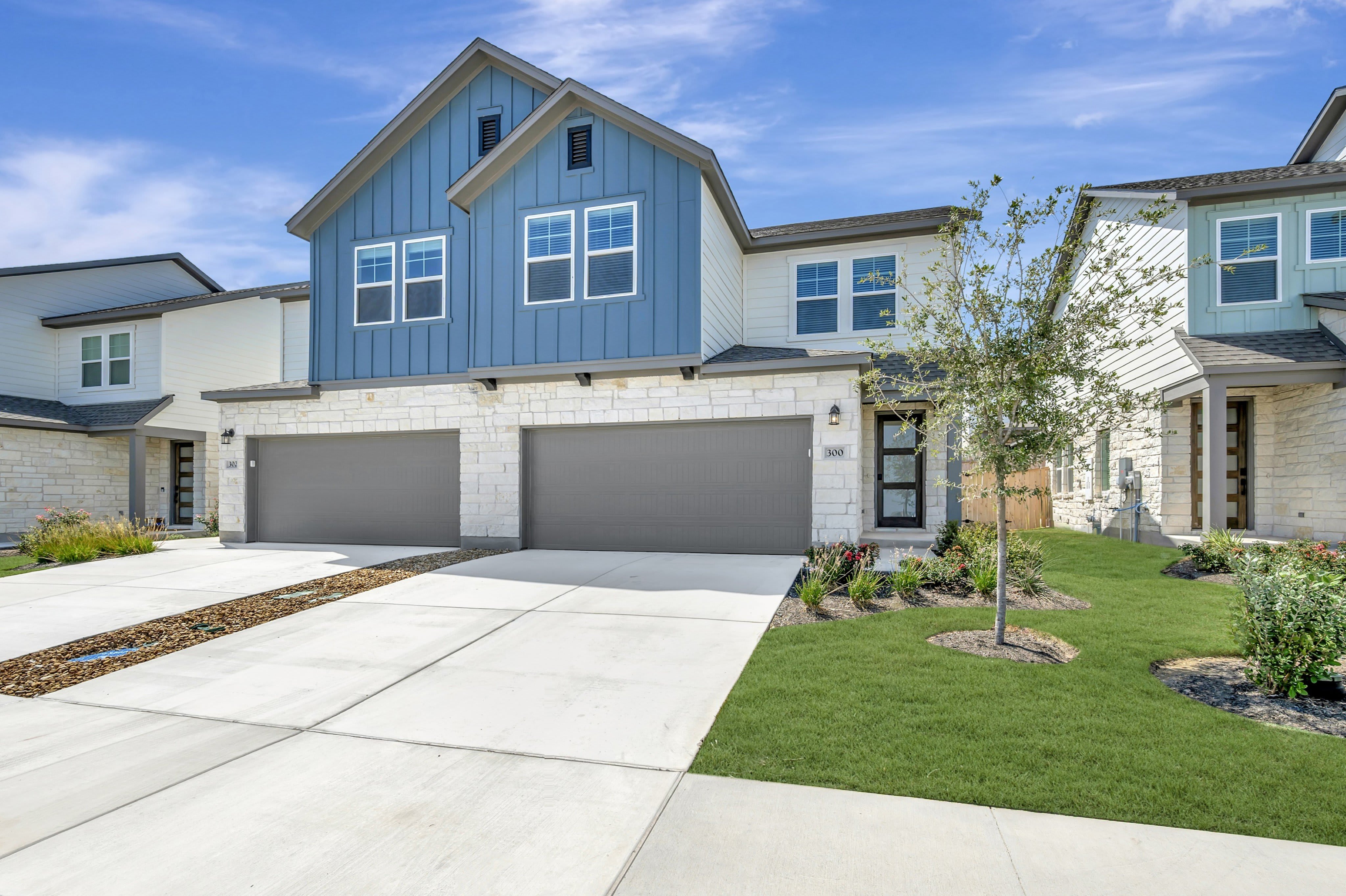 A modern townhouse with a blue and white exterior and a manicured lawn sits under a bright blue sky.