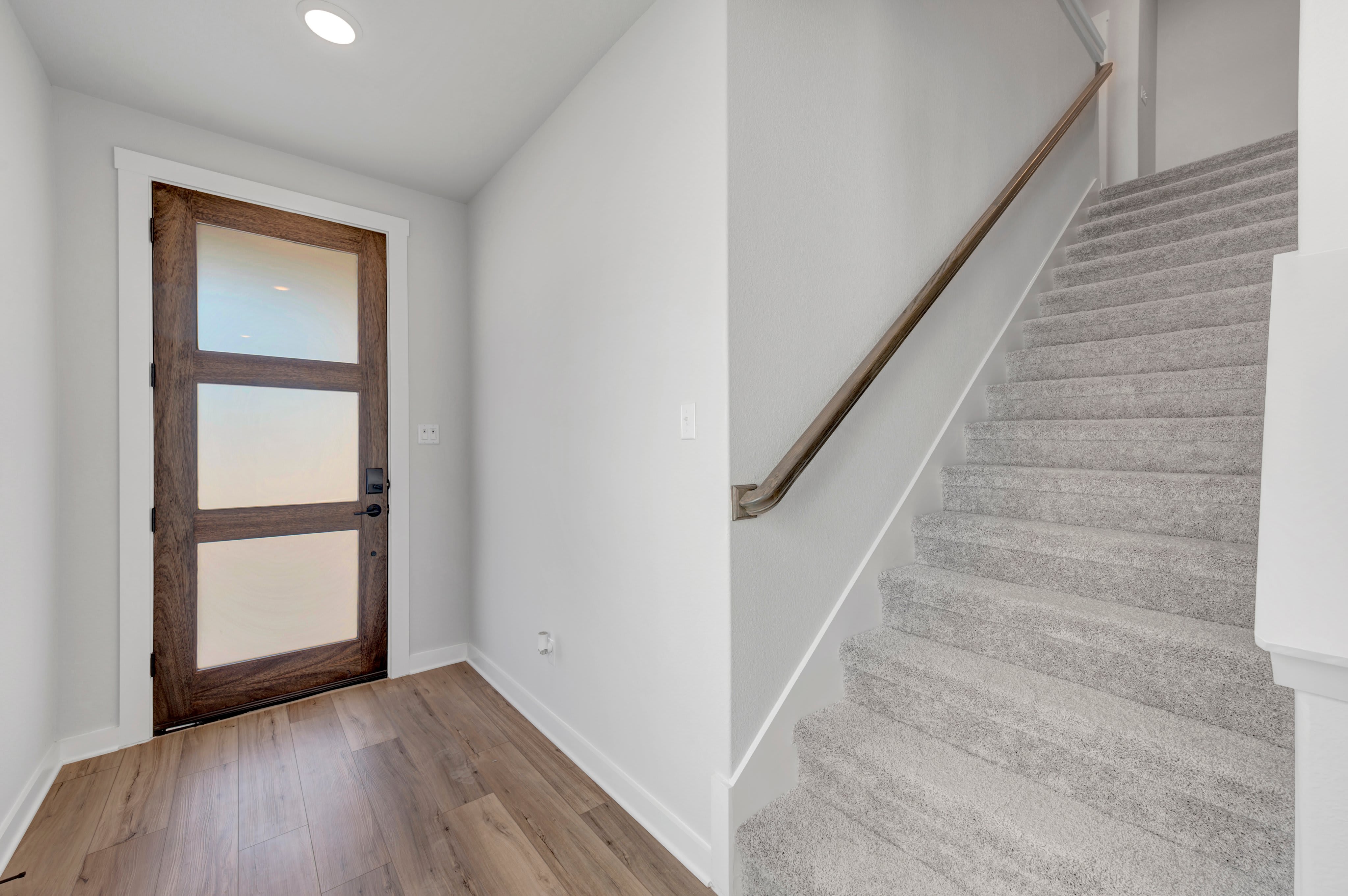 A modern wooden door with frosted glass panels stands in the foreground, leading to a carpeted staircase in the background.