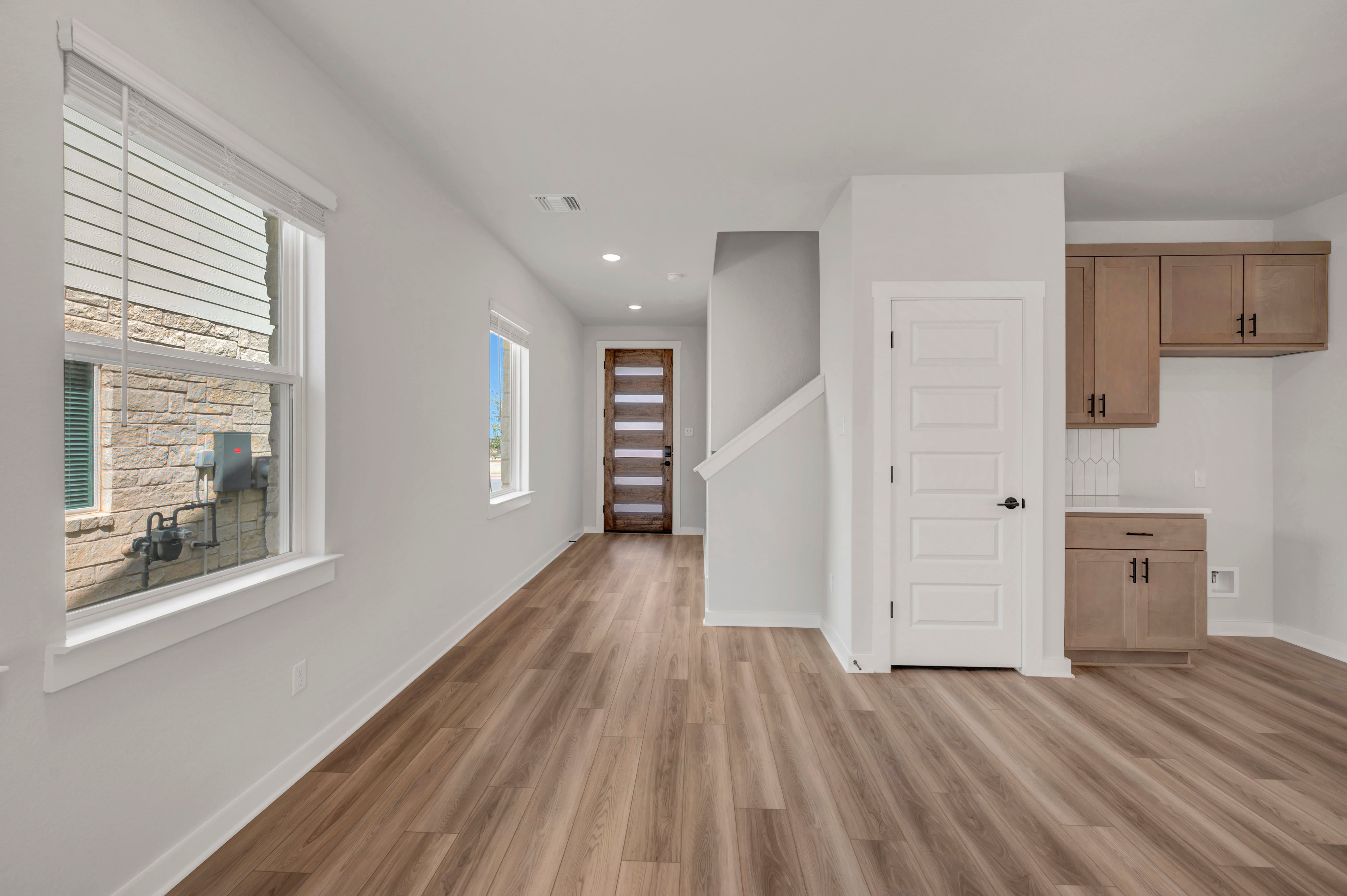 A modern living space with a wood-look floor in the foreground and a staircase and kitchen cabinets in the background.