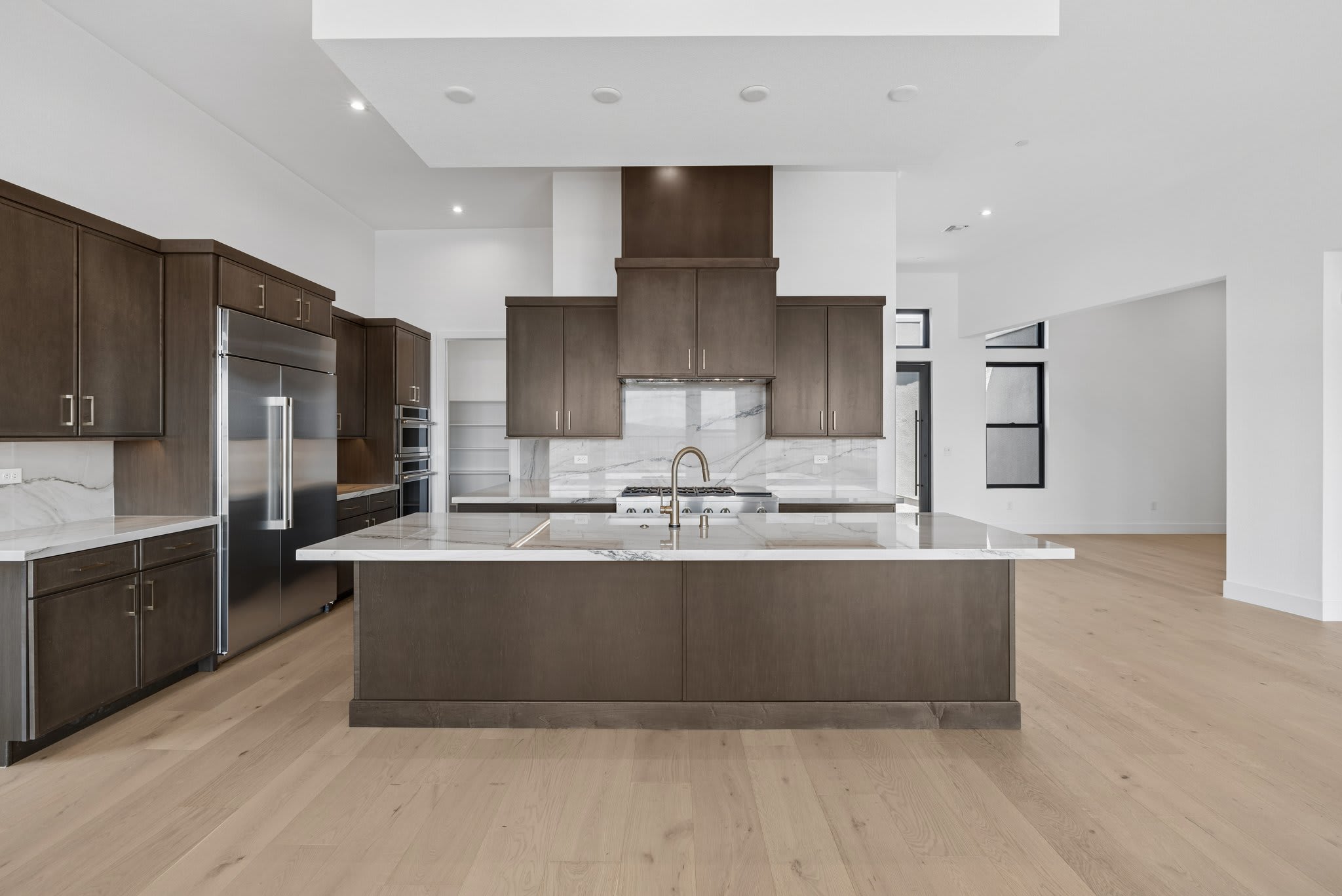 A modern, spacious kitchen with a large island in the foreground and a bright, open living area in the background.