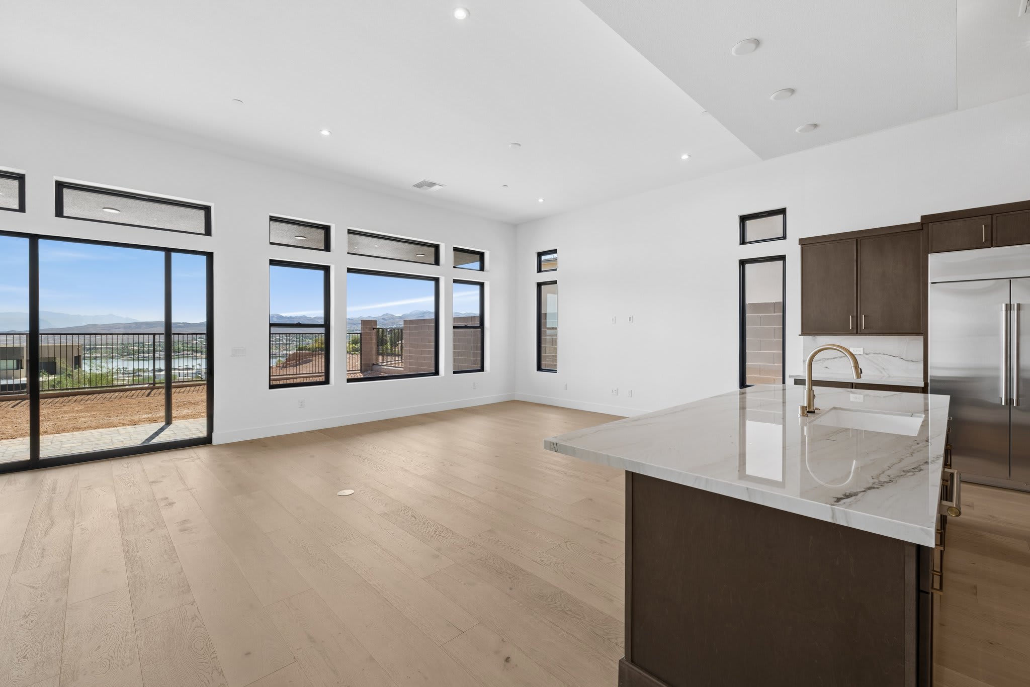 A modern kitchen island with a marble countertop is in the foreground, while a spacious living area with large windows offering a scenic view of a distant landscape is in the background.