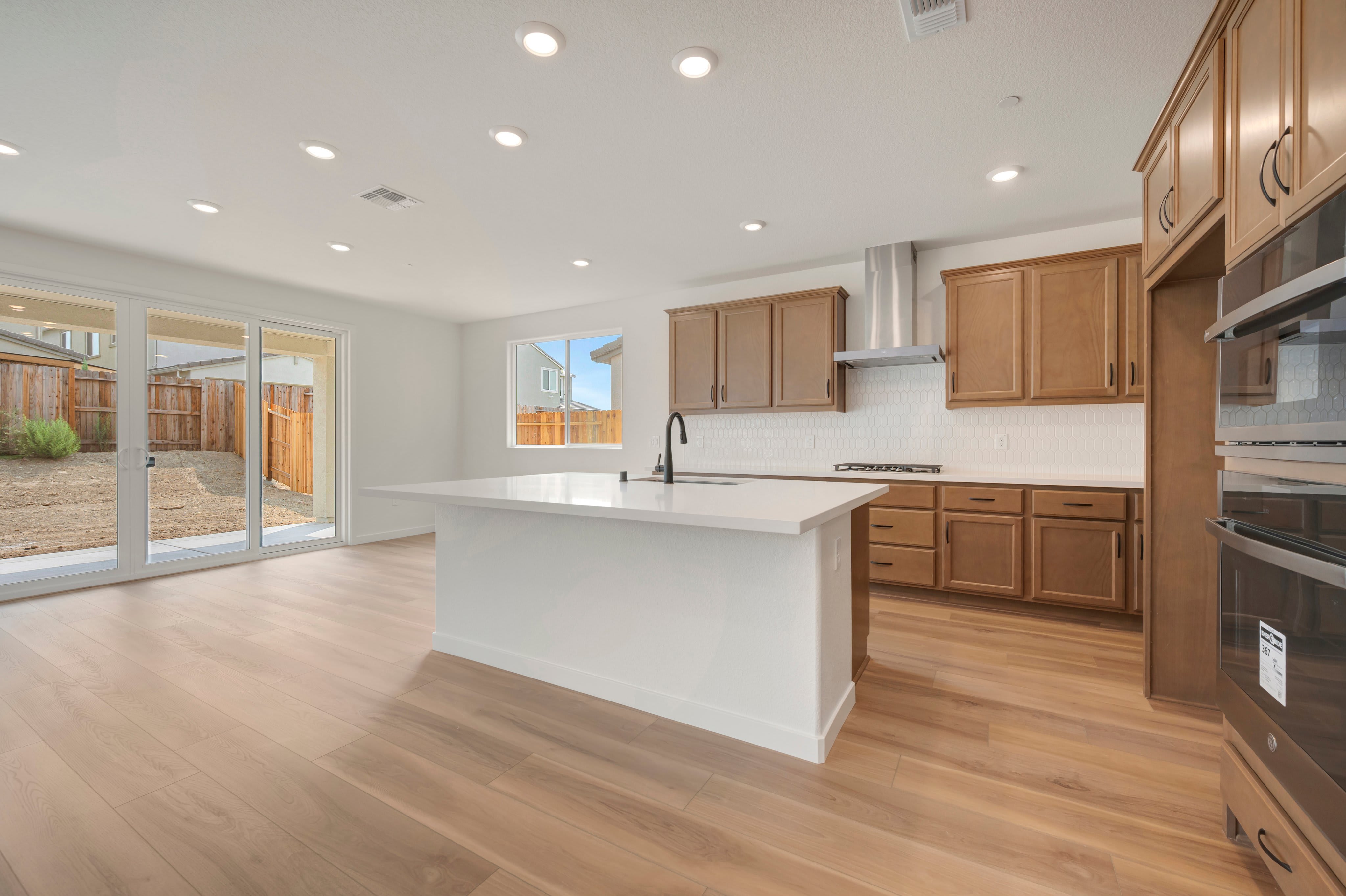 A modern kitchen with a white island in the foreground opens to a backyard with a wooden fence in the background.
