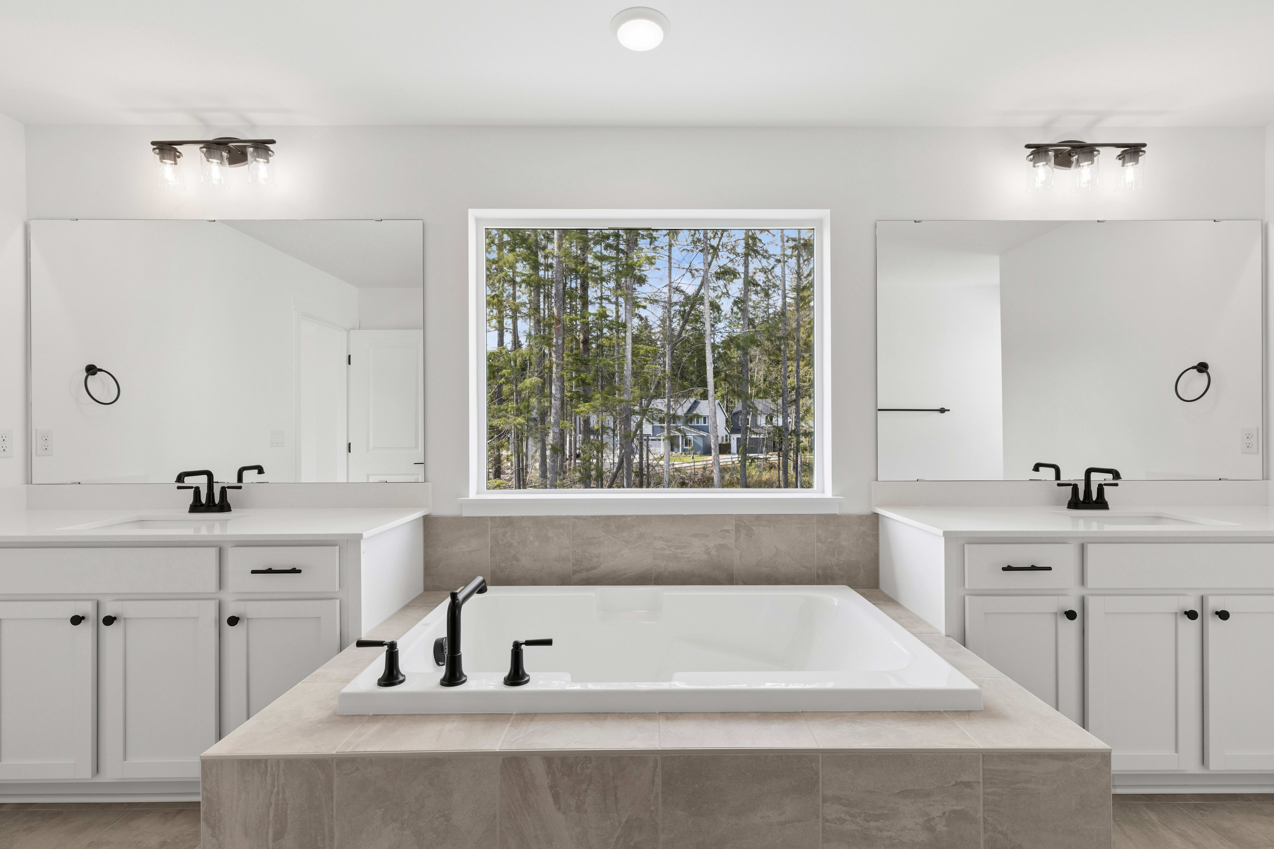A modern bathroom with a large soaking tub in the foreground and a window overlooking a wooded area in the background.
