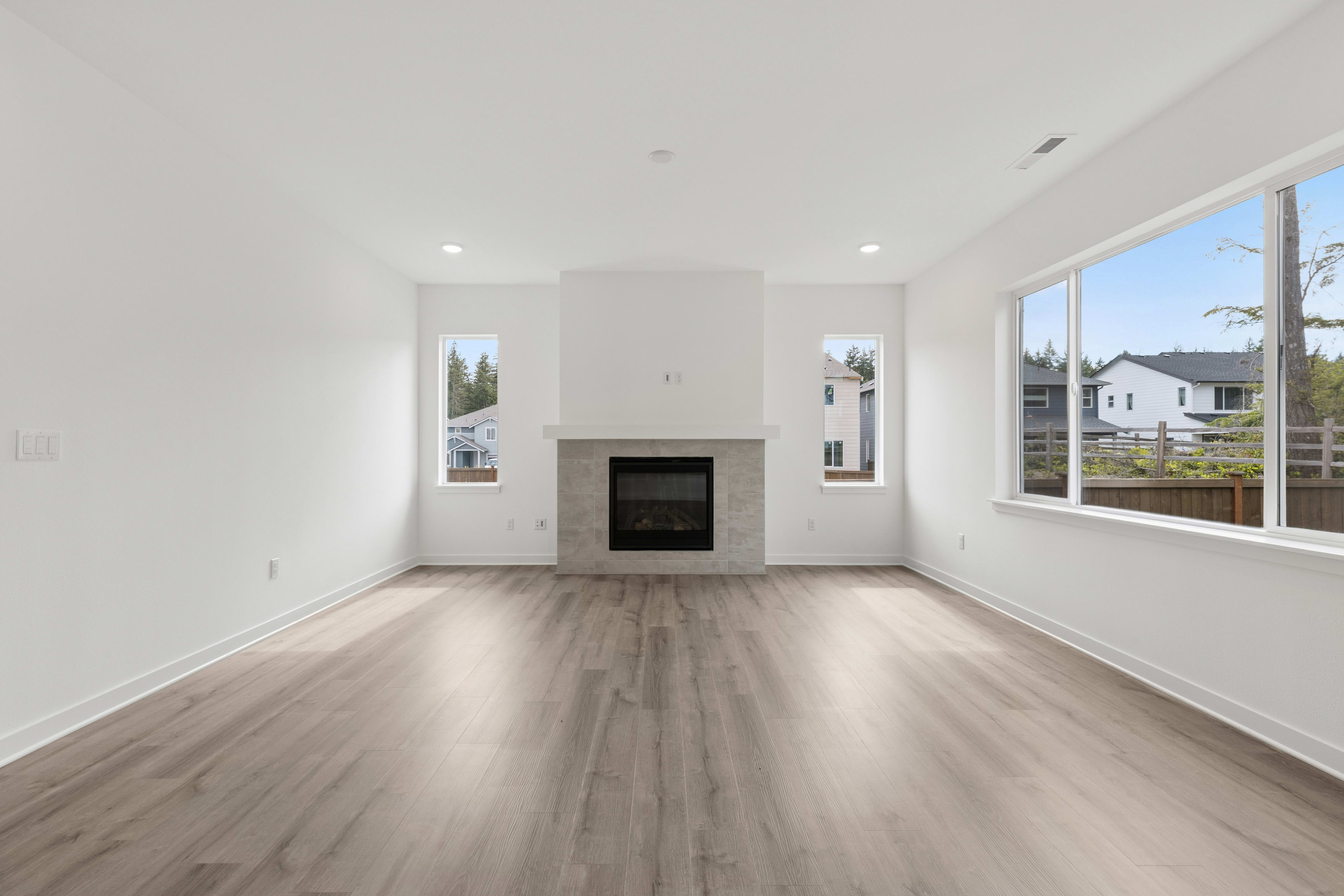 A modern living room with a gray fireplace and large windows overlooking a suburban neighborhood.