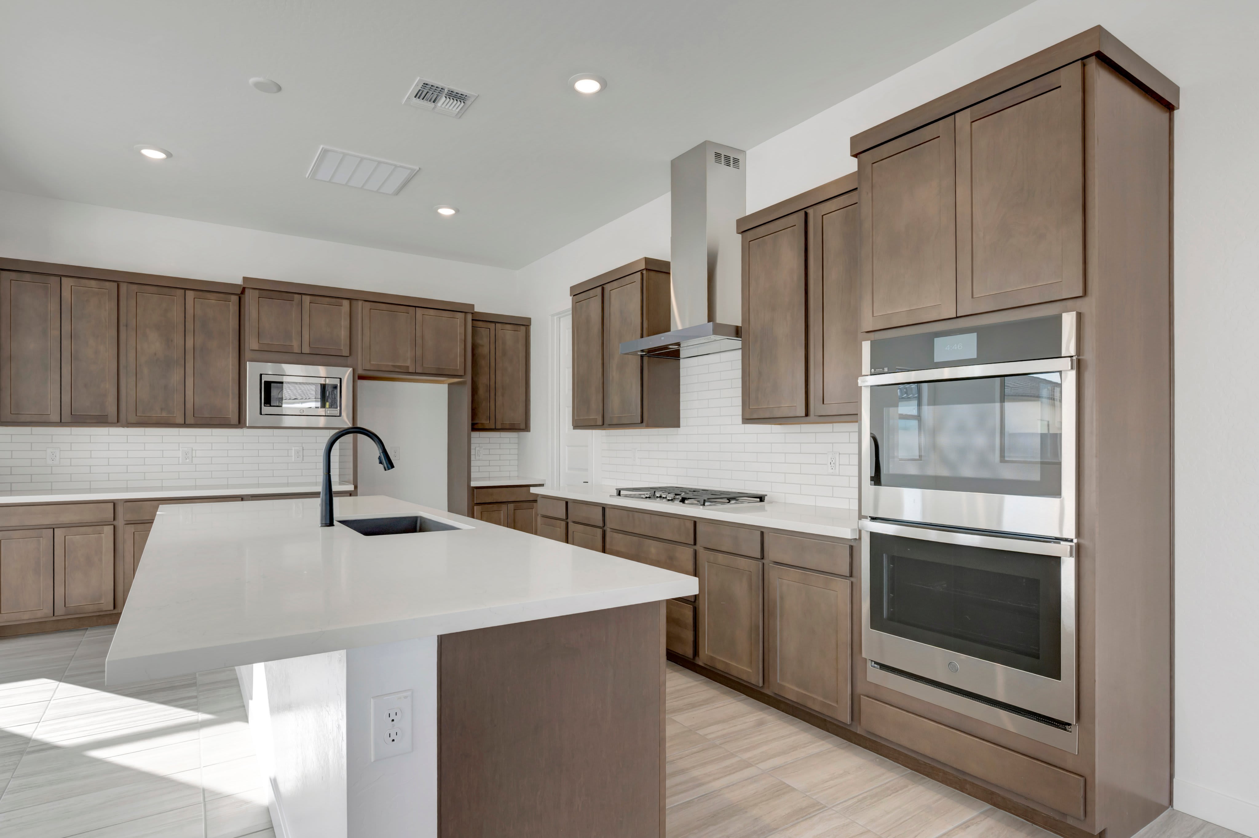 A modern kitchen with a large island in the foreground and dark wood cabinets and stainless steel appliances in the background.