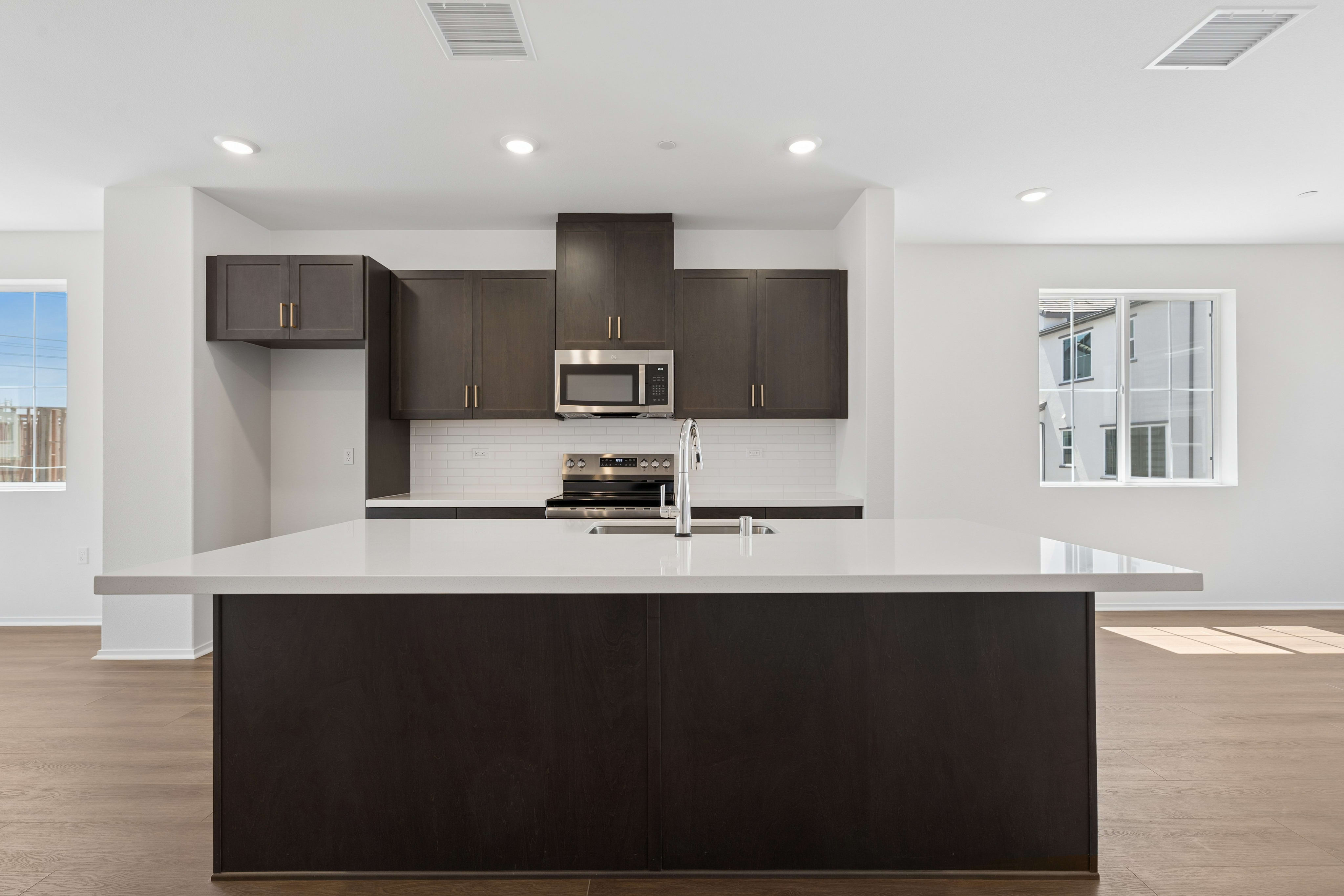 A modern kitchen with a dark island in the foreground and dark cabinetry with stainless steel appliances in the background.