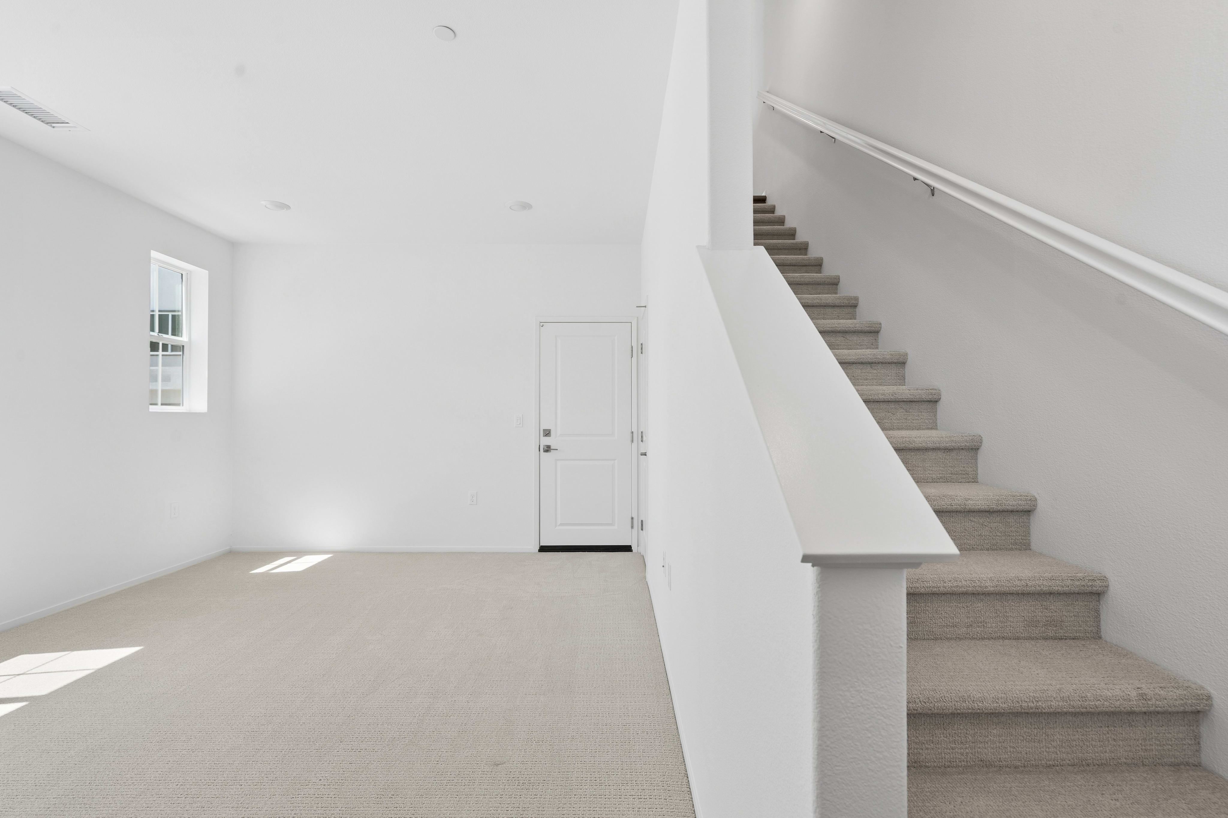 A carpeted room with a white door and window in the background is dominated by a carpeted staircase in the foreground.