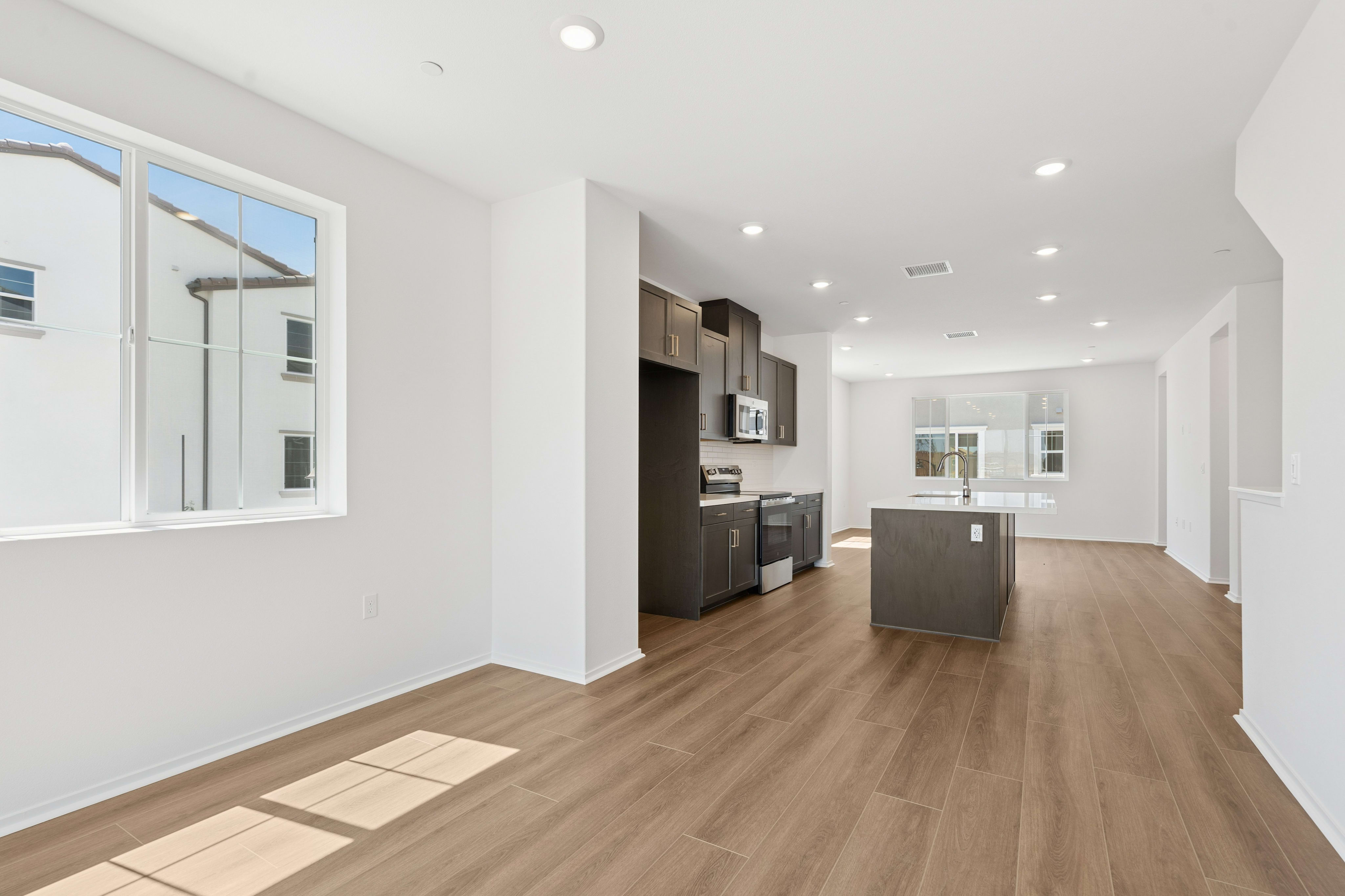 A bright, modern living space with a large window in the foreground and a sleek kitchen with an island in the background.
