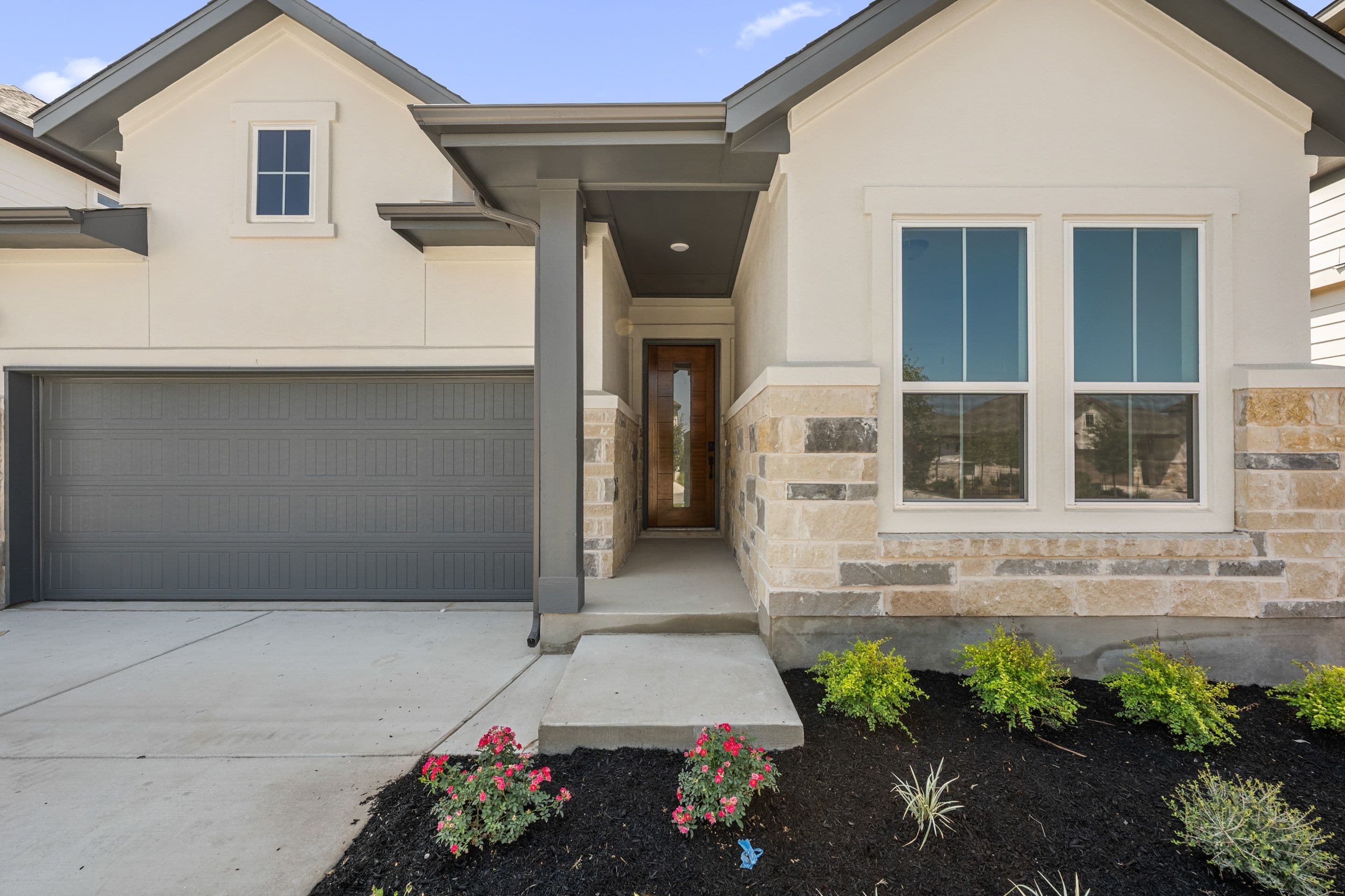 A modern house with a gray garage door and stone accents in the foreground is set against a clear blue sky in the background.