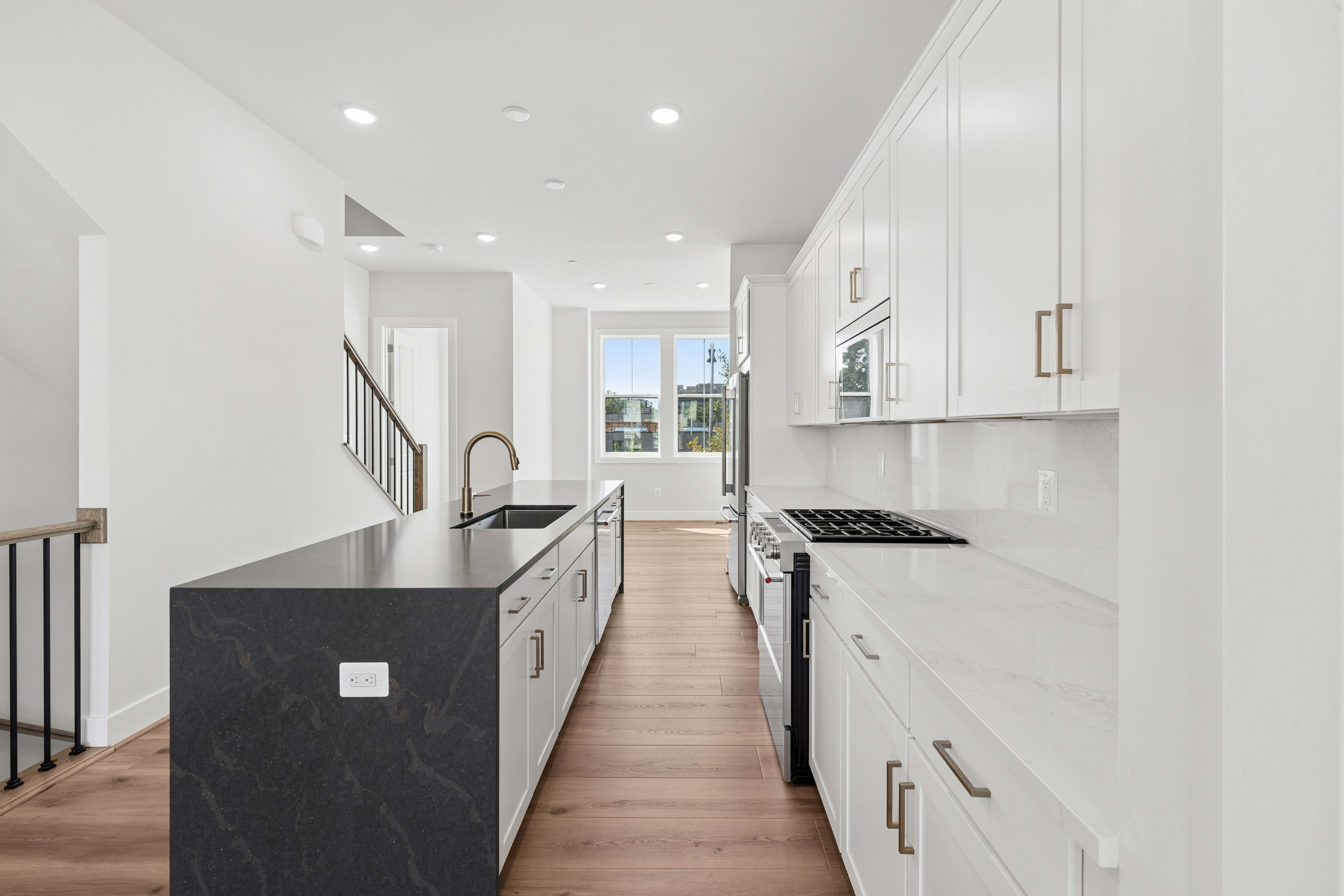 A modern kitchen with a dark island in the foreground and white cabinetry and appliances in the background.